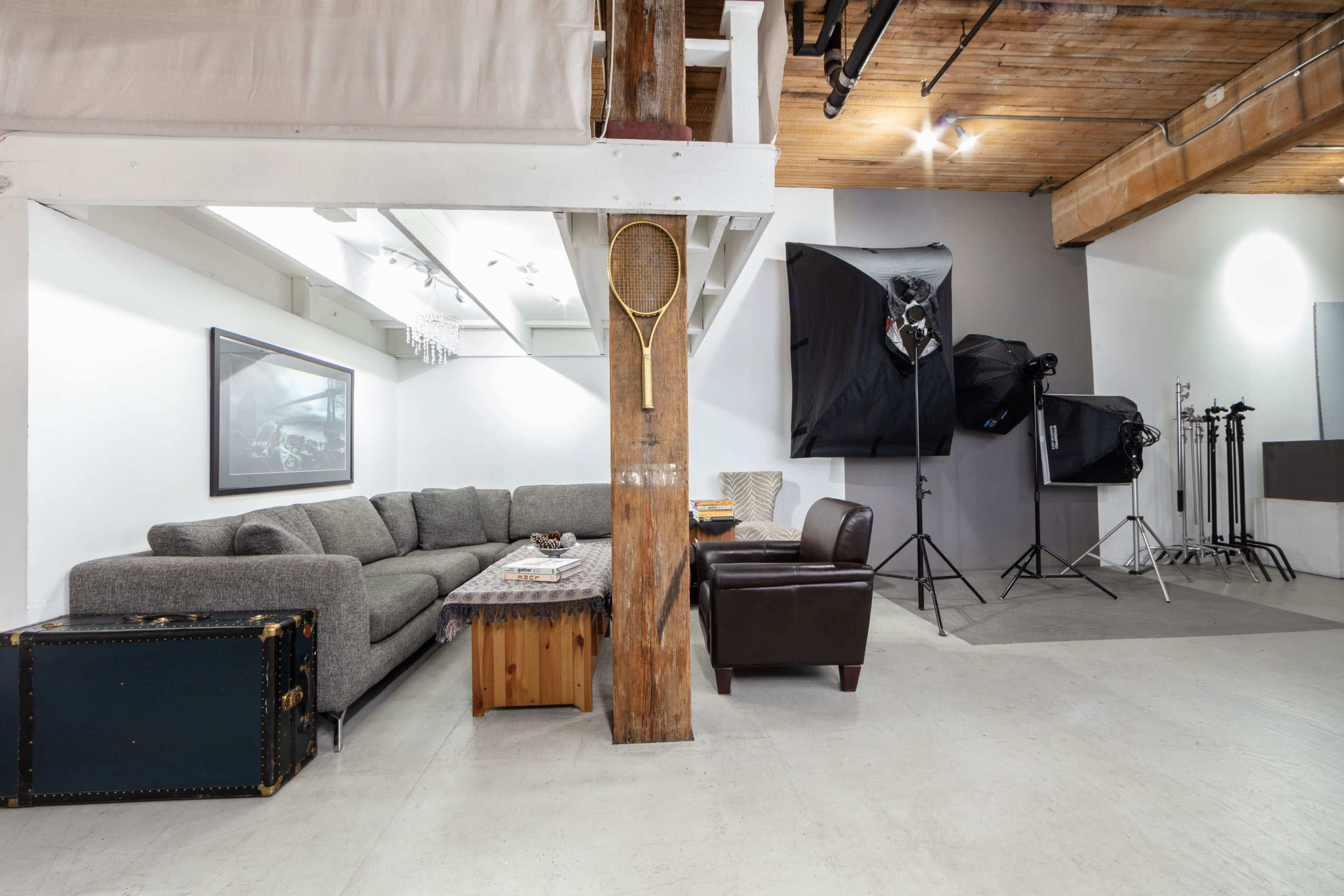 A spacious living area featuring a gray sectional sofa, a wooden coffee table, and photography equipment in the background.