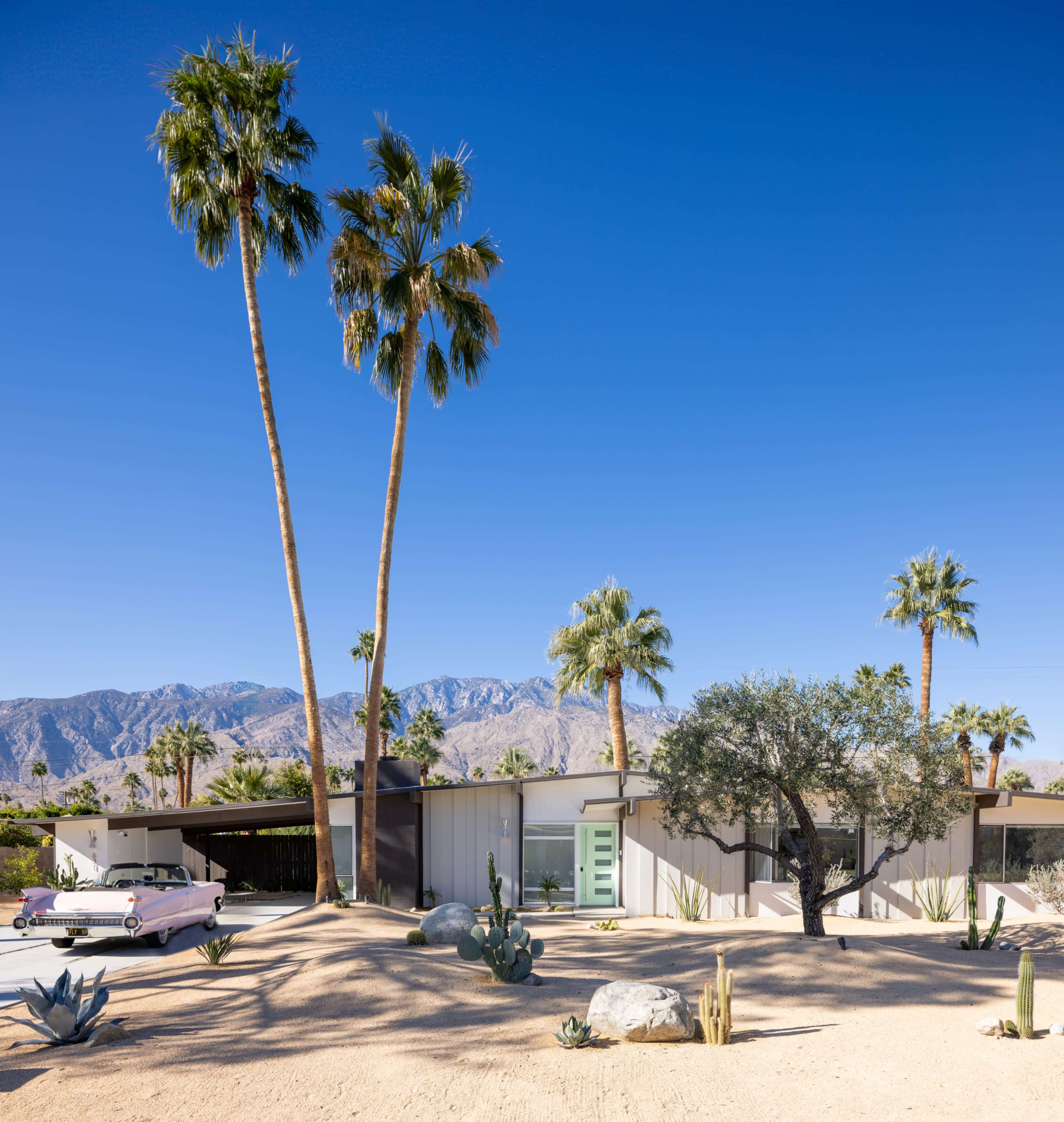 The image shows a modern house surrounded by desert landscaping and palm trees, with mountains visible in the background.