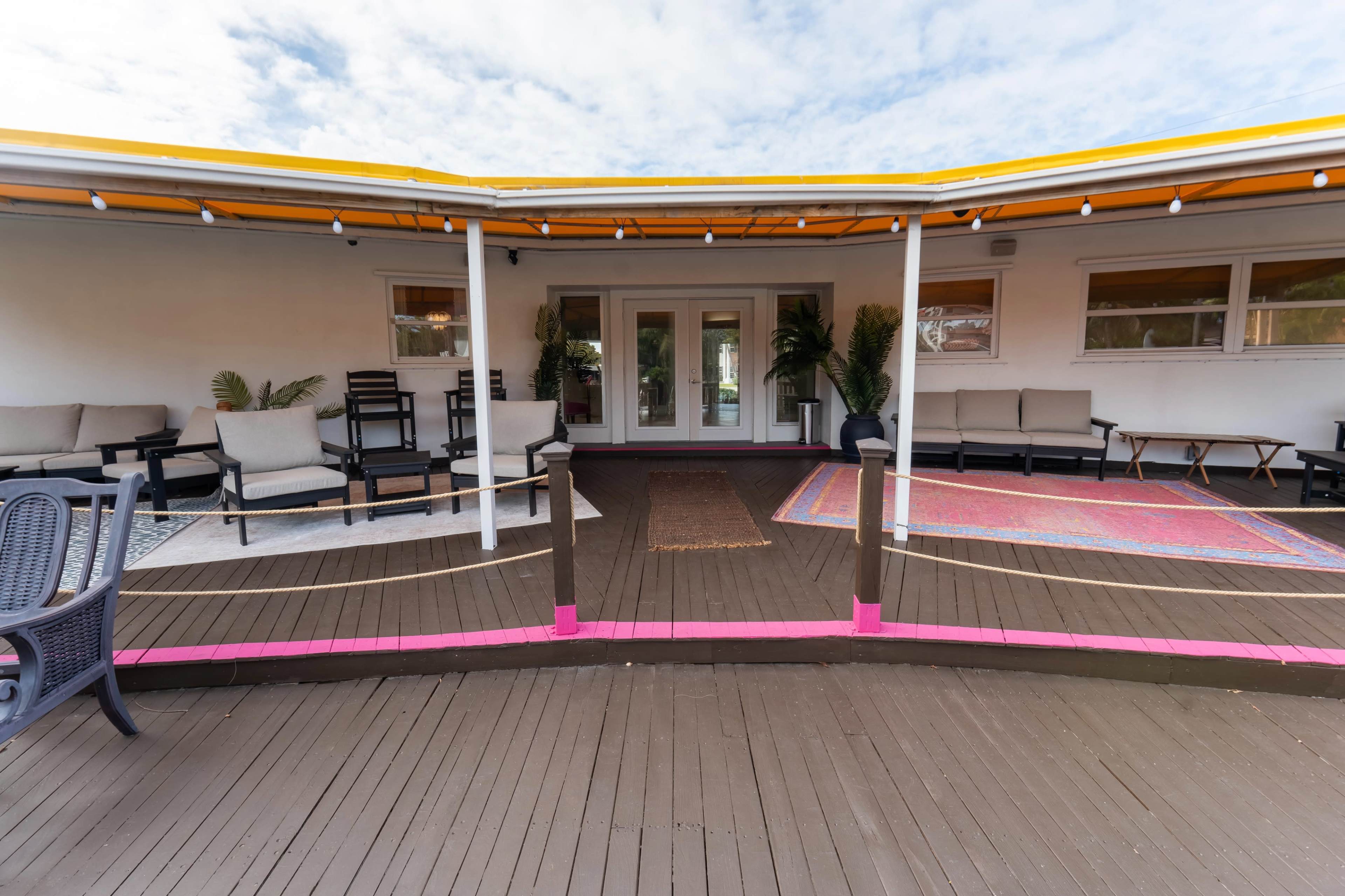 The image shows a flat, outdoor patio area with multiple seating options and a vibrant orange canopy overhead.