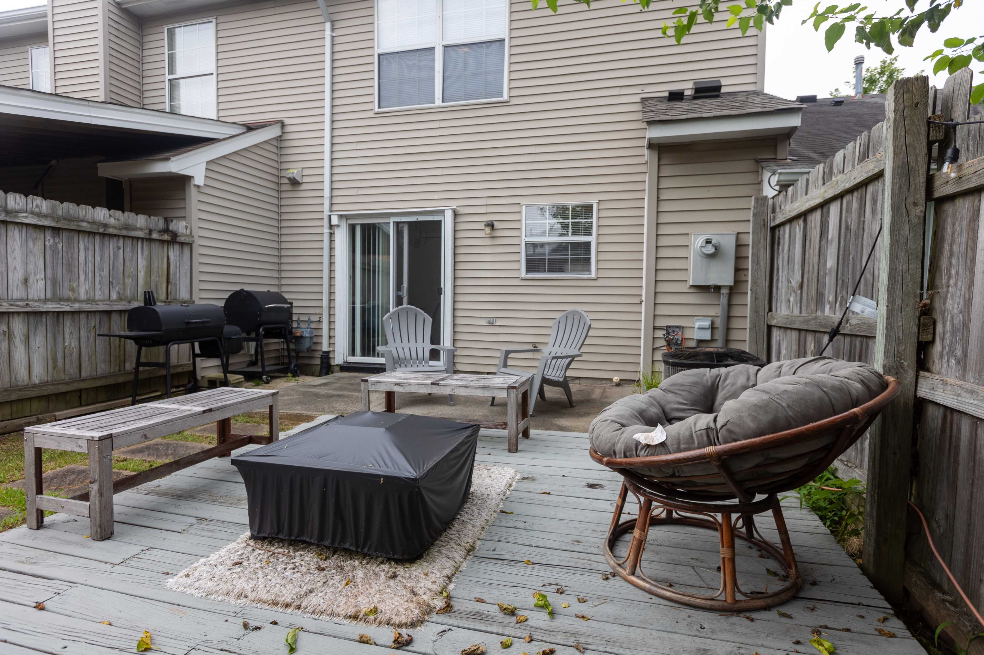 A backyard patio with wooden decking, featuring a circular chair, a small table, and a grill in the background.