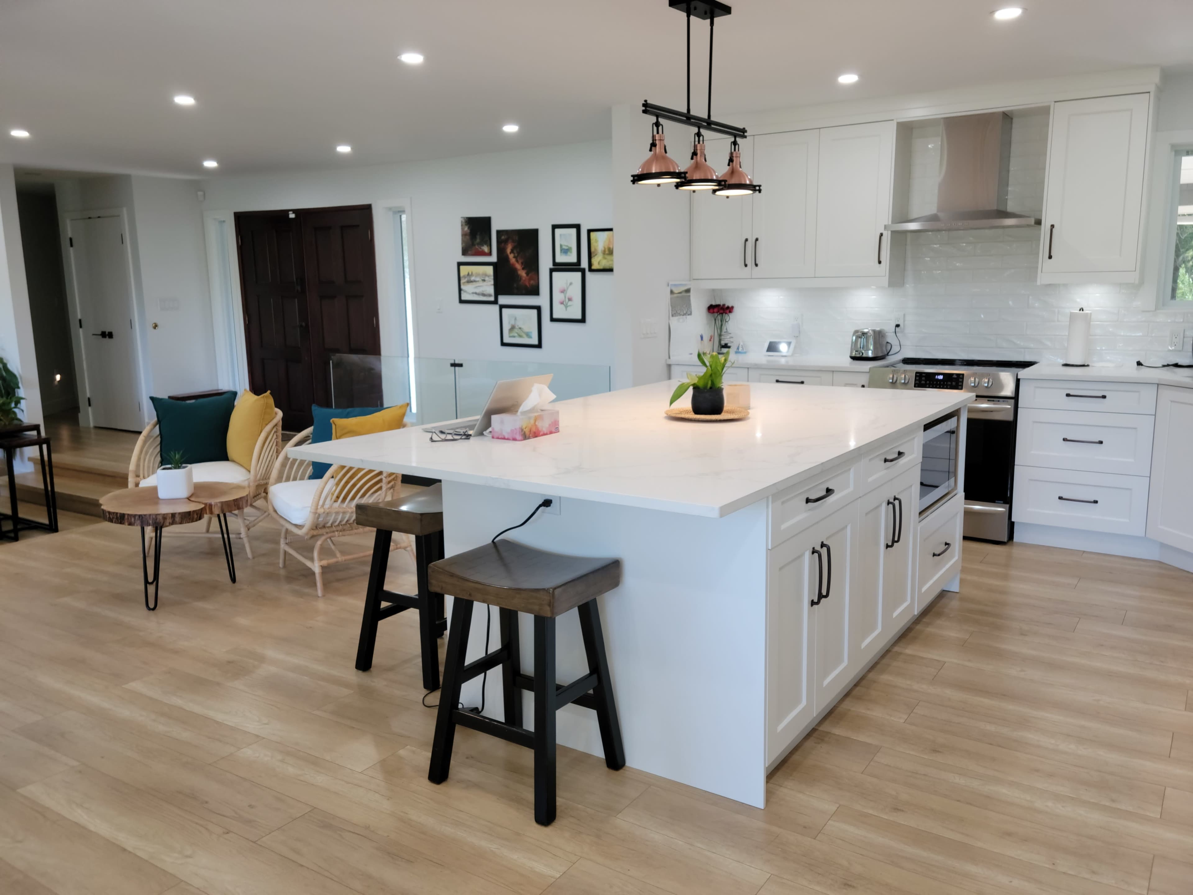 A modern kitchen with a large island, featuring white cabinetry, stainless steel appliances, and a dining area with various seating options.