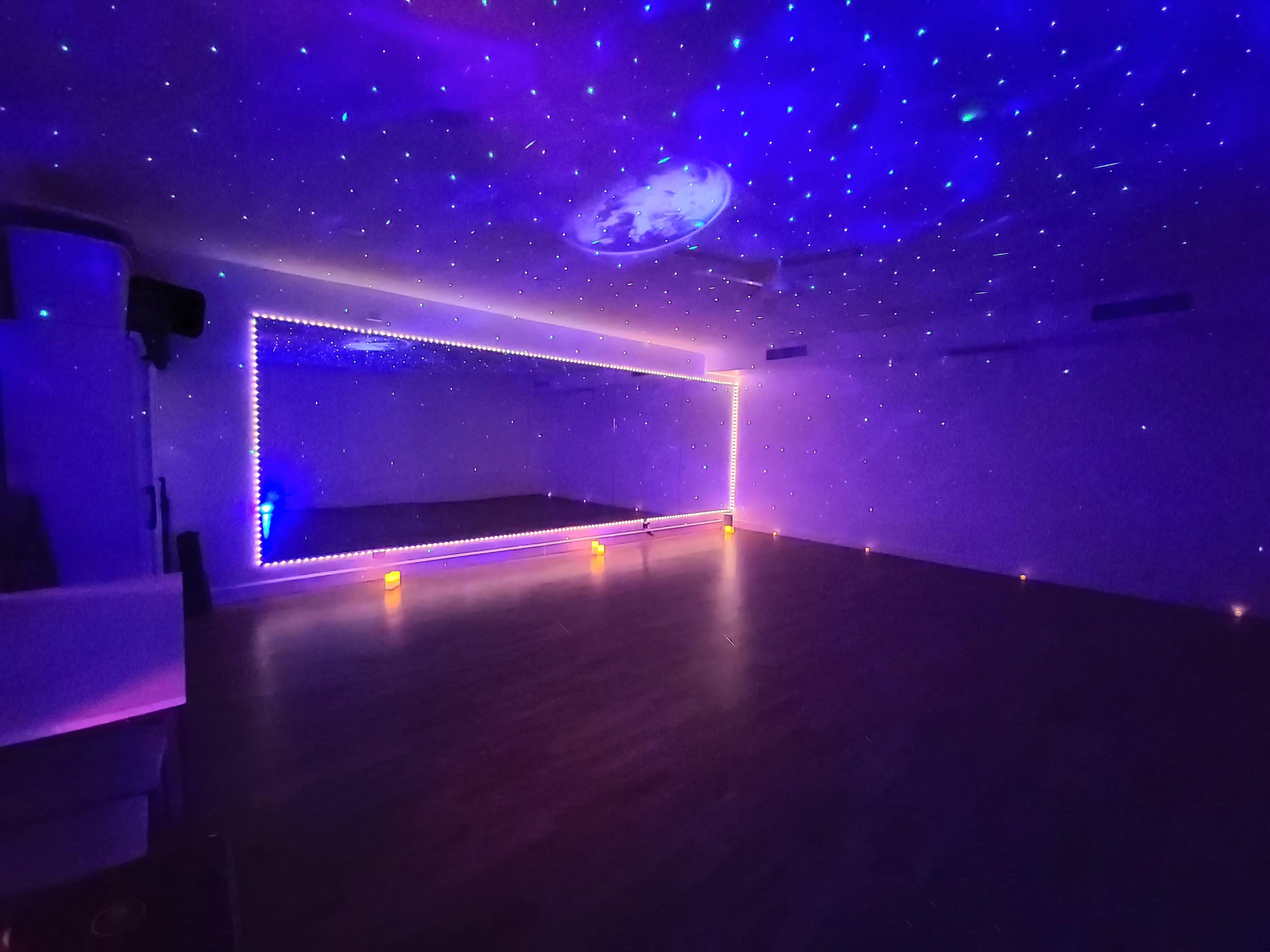 A spacious room features a large mirror along one wall and a ceiling decorated with a starry projection, illuminated by soft lights.