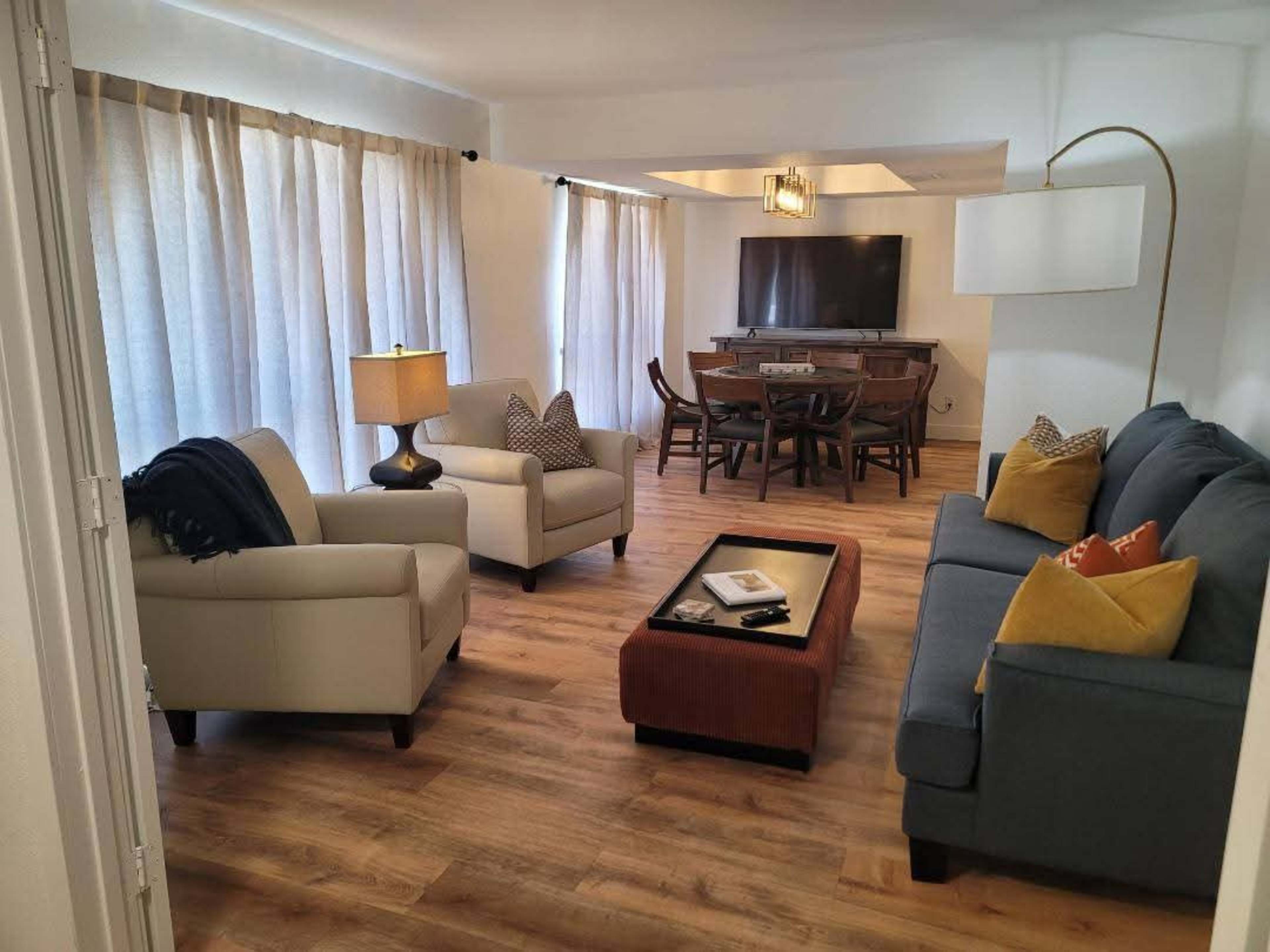 The image shows a living room with two armchairs, a sofa, a coffee table, and a dining area with a television.