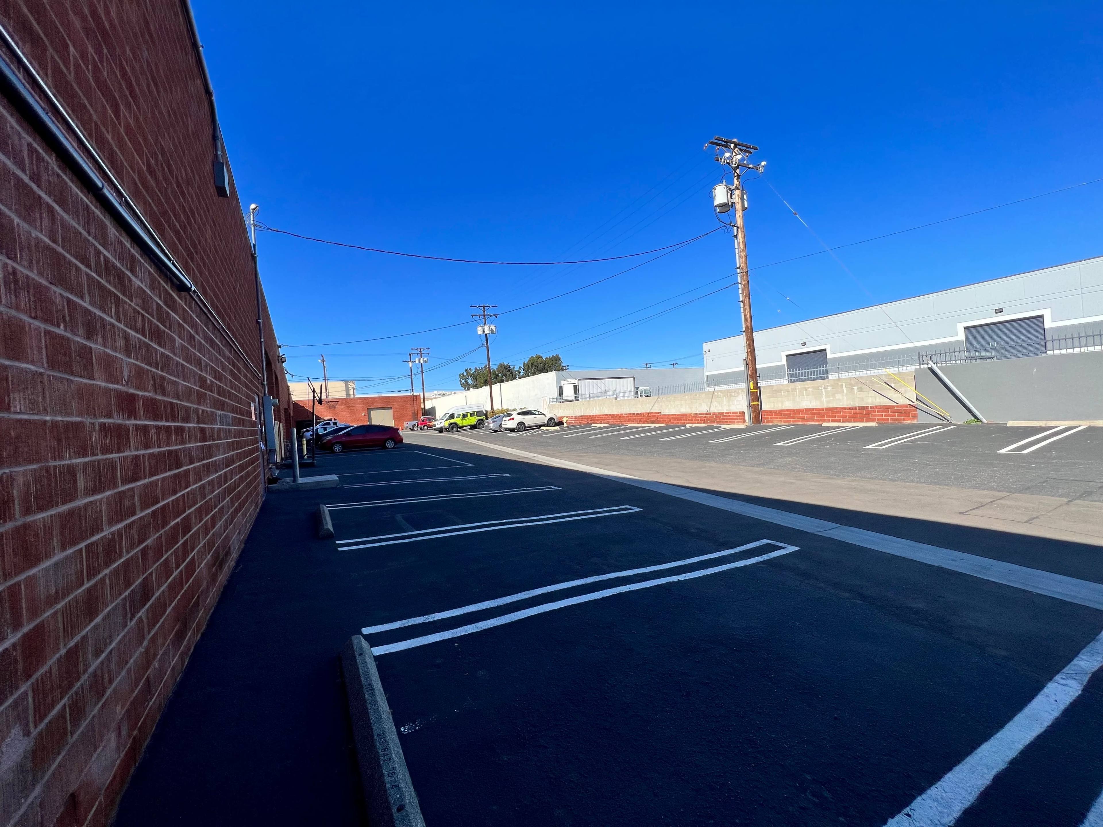 A parking lot alongside a brick building, with empty spaces and a clear blue sky overhead.