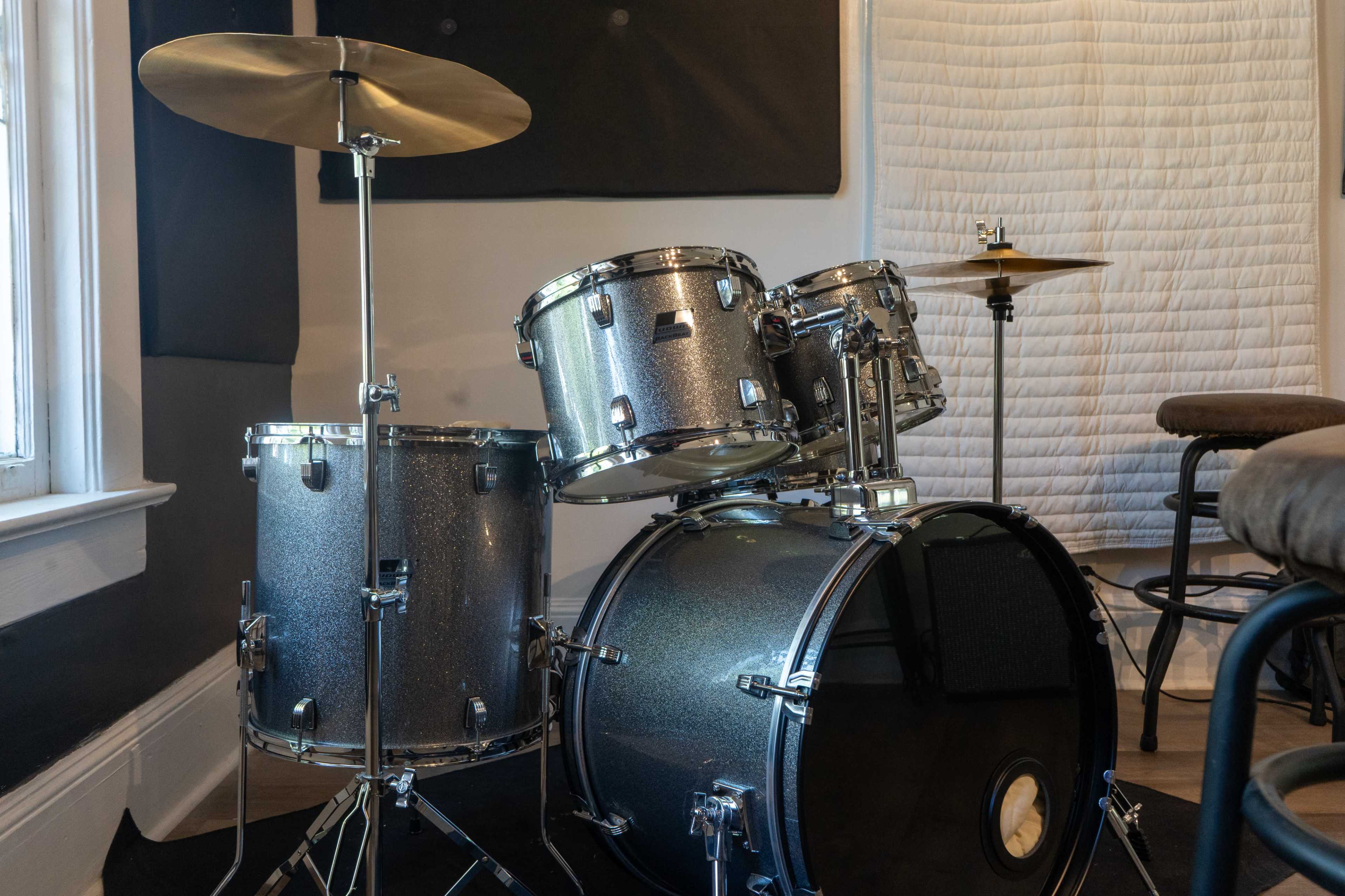 A silver drum kit with a bass drum, snare, toms, and cymbal is positioned in a well-lit room.
