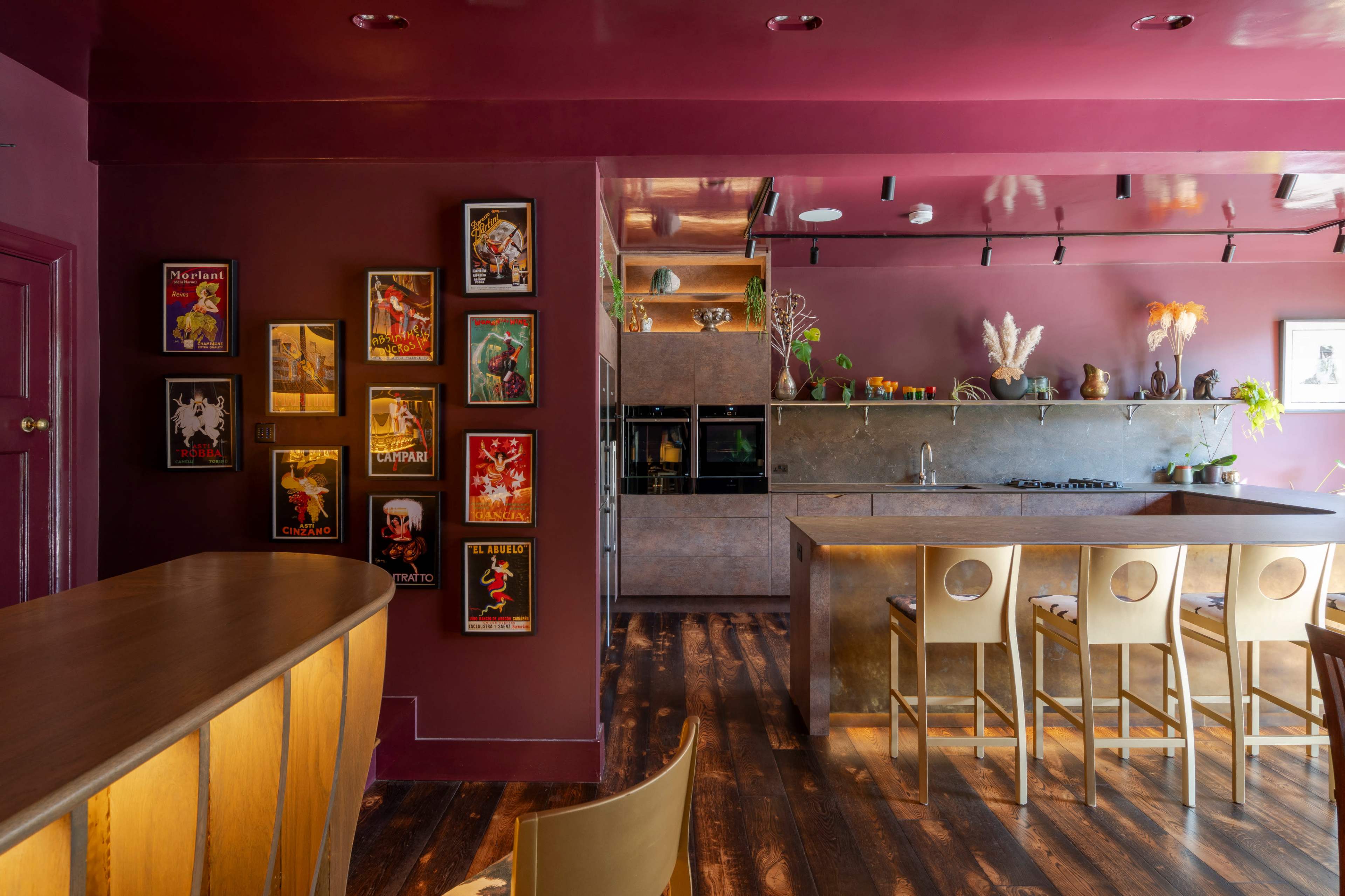 A stylish interior of a restaurant or café featuring a maroon color scheme, modern kitchen appliances, and framed artwork on the walls.