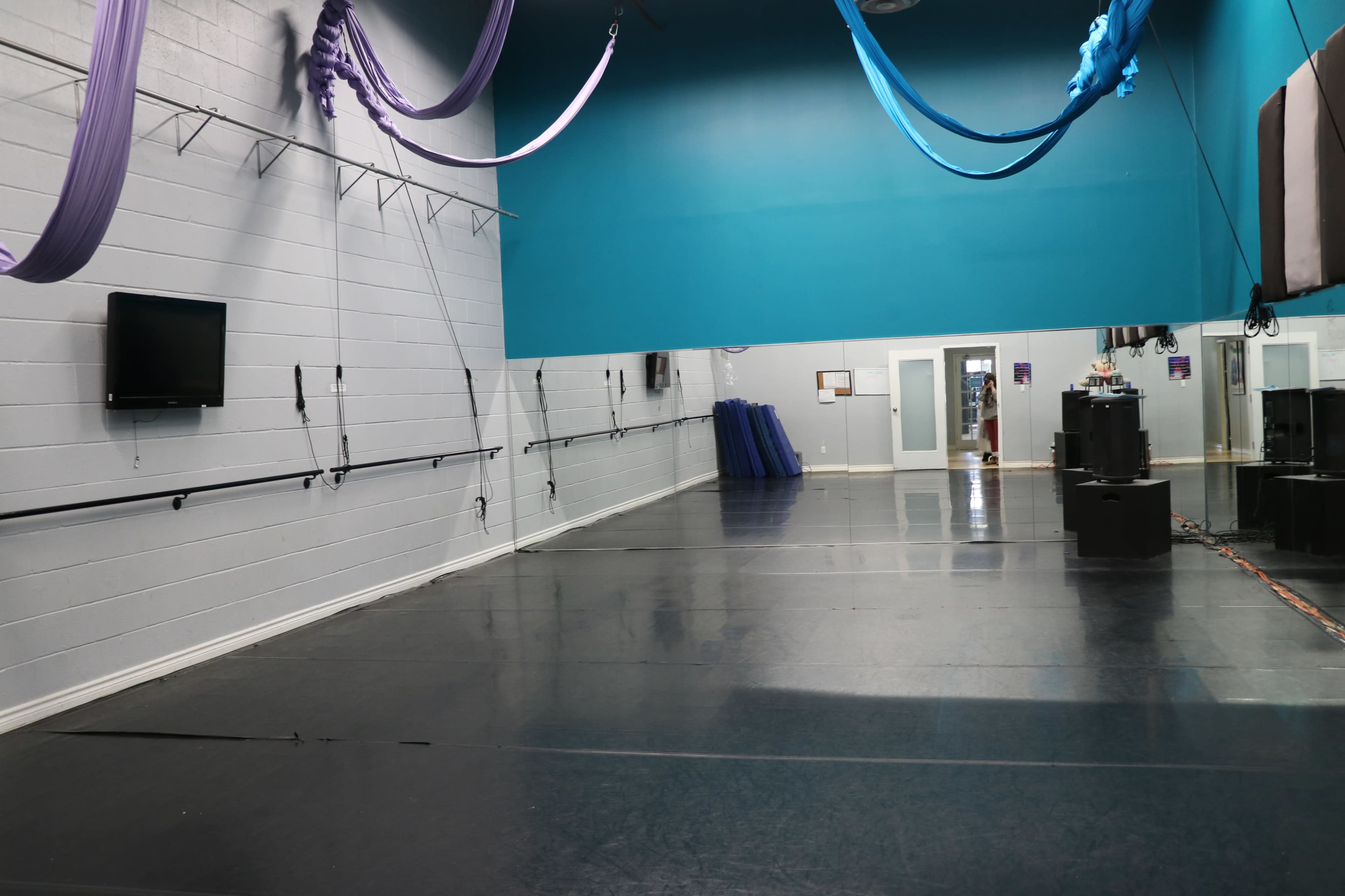 The image shows an empty gymnasium with a dark floor, blue walls, and suspended fabric for aerial performances.