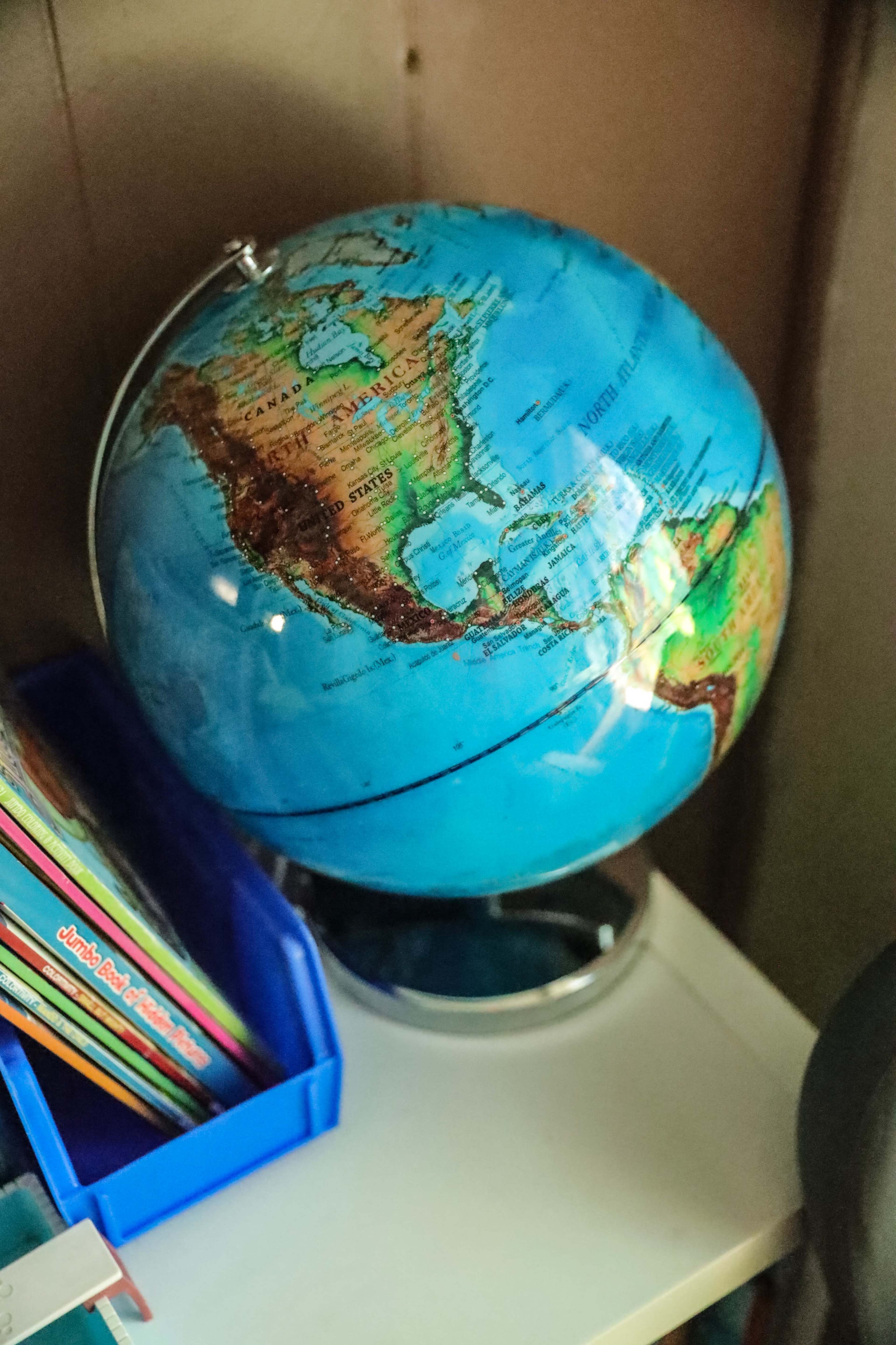 A colorful globe depicting the Americas sits on a white shelf beside a blue container holding books.