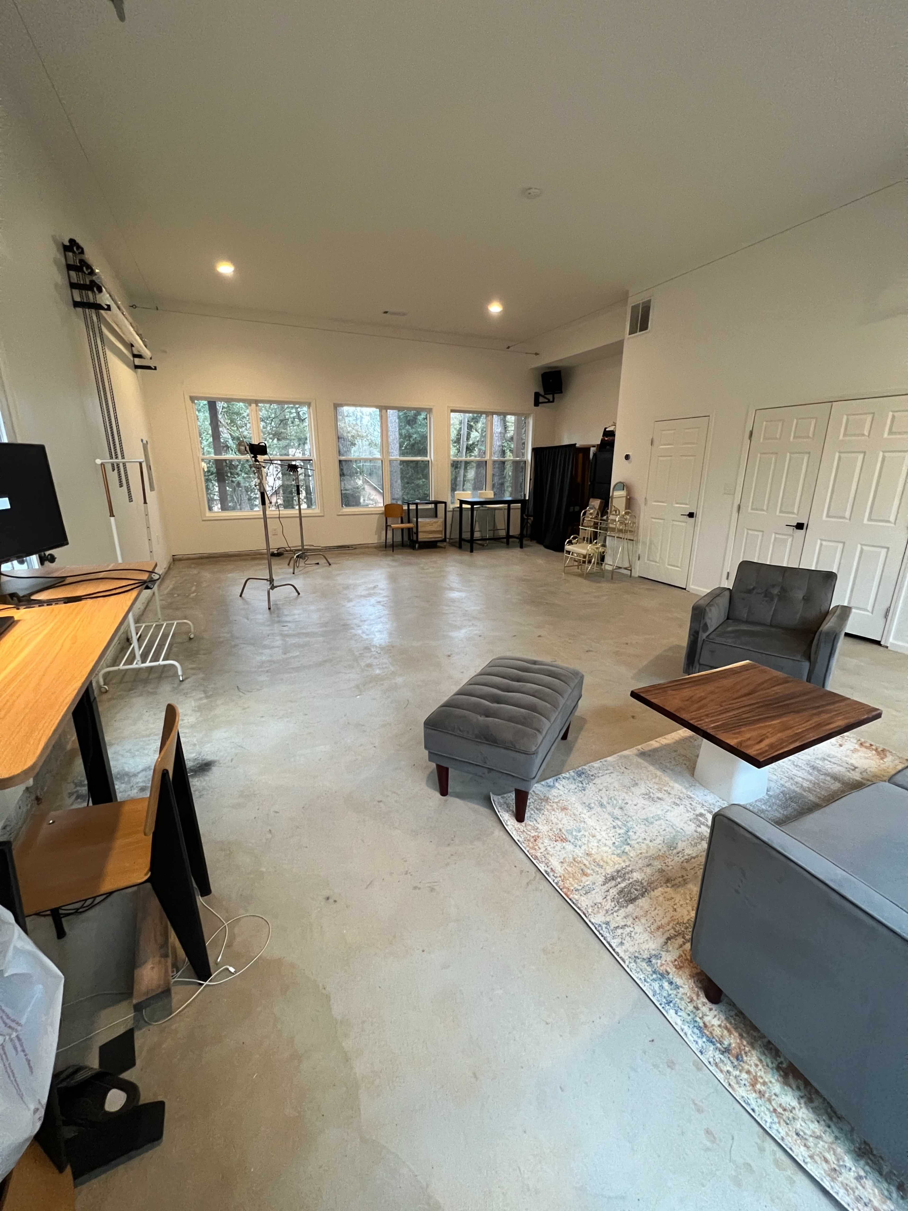 A spacious room with wood accents, large windows, and minimal furniture, including a sofa, ottoman, and two tables.