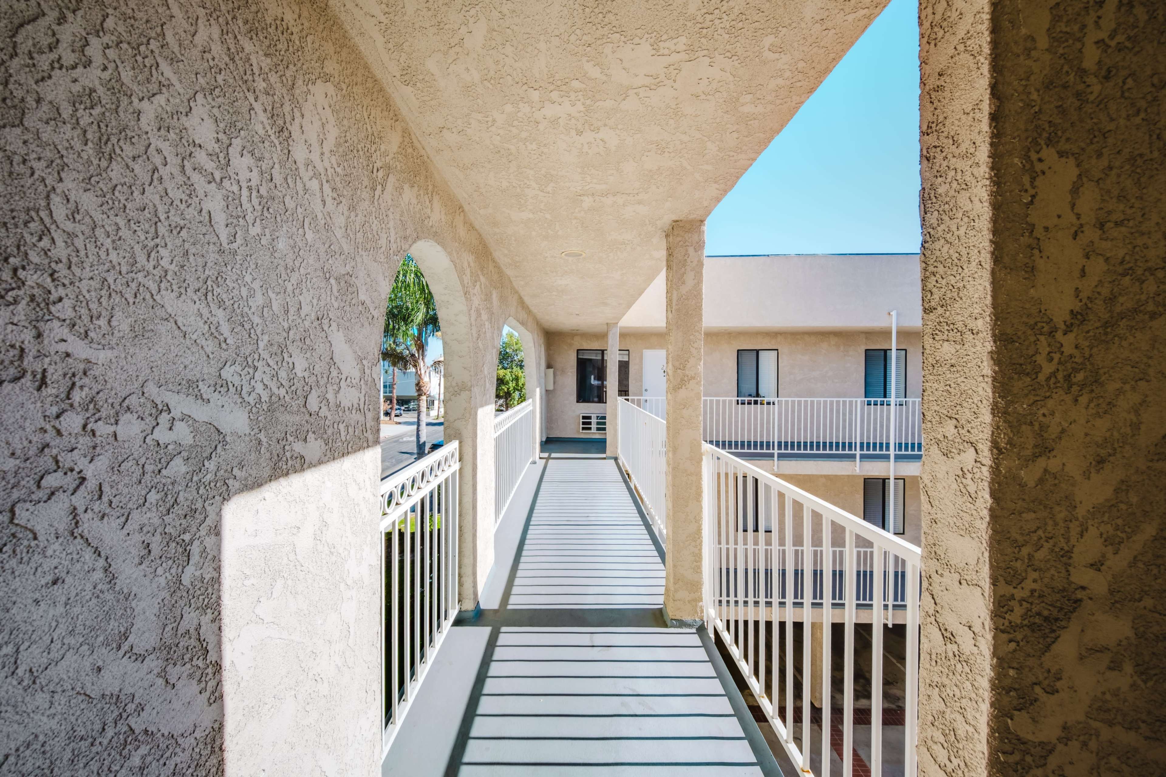 The image shows a brightly lit exterior corridor of a multi-story building with arches and a view of the surrounding area.
