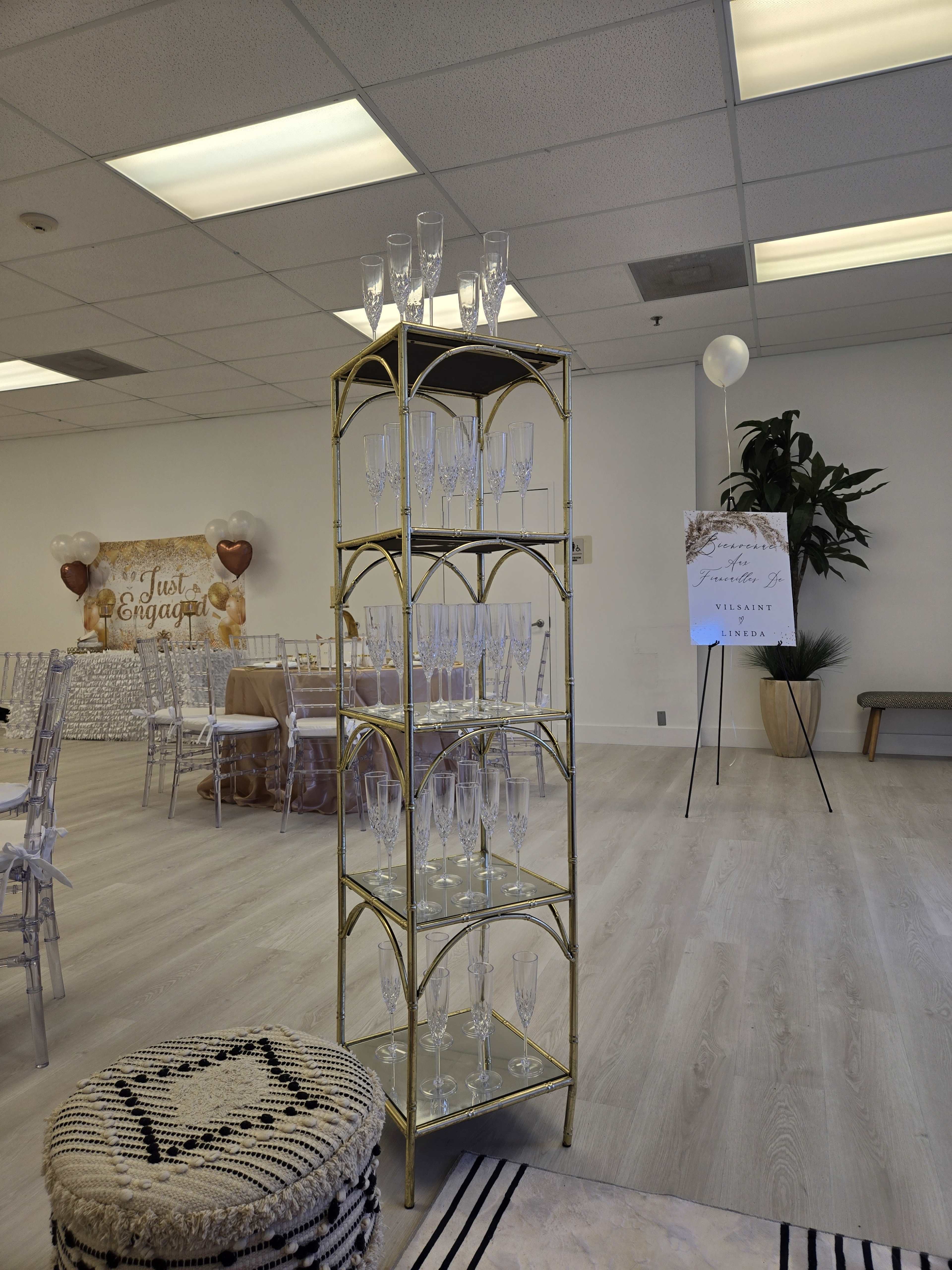 A gold-framed shelving unit displays several stacked champagne flutes in a decorated event space.