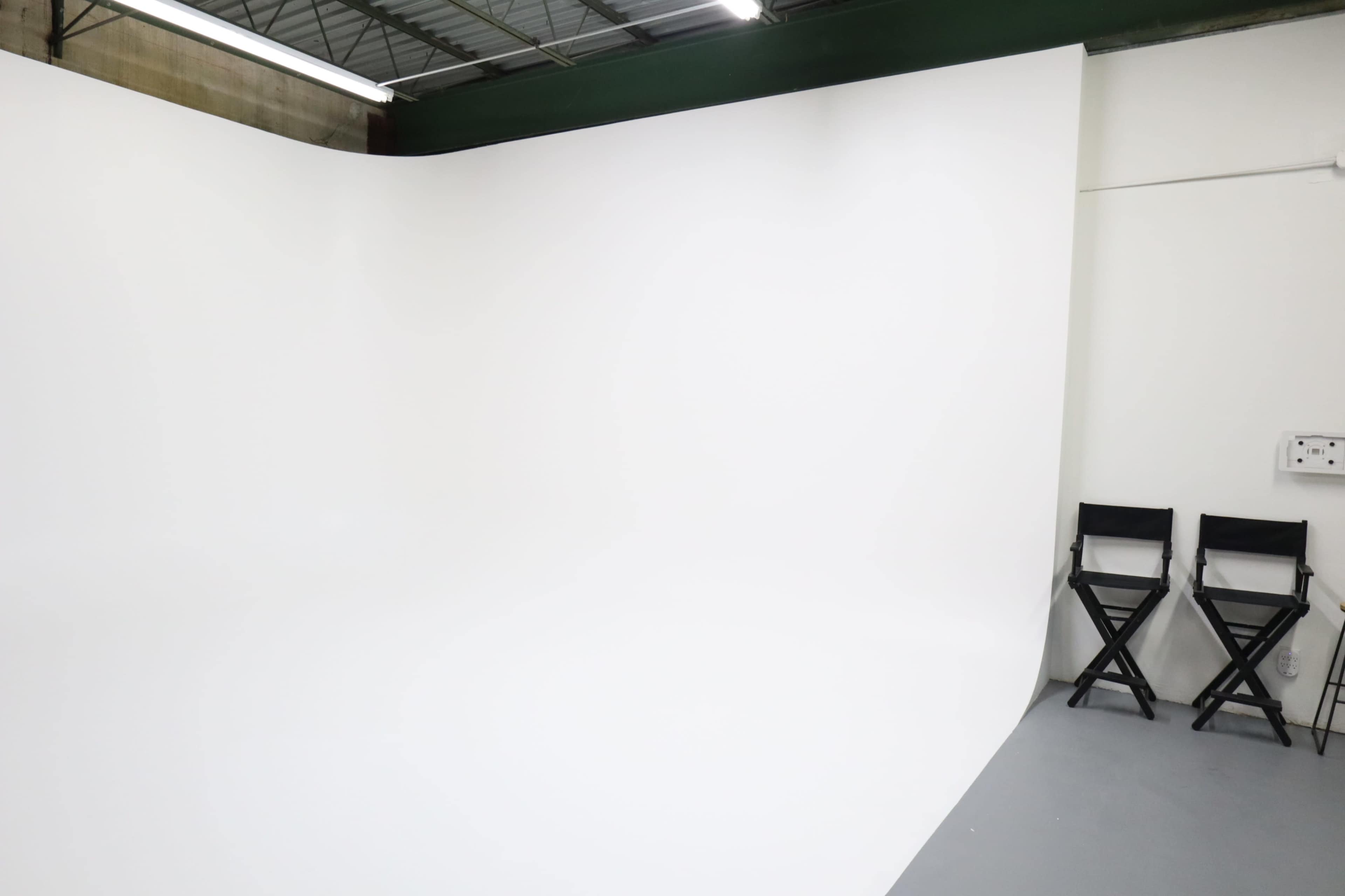 A minimalist photo studio with a white backdrop and two black director's chairs.
