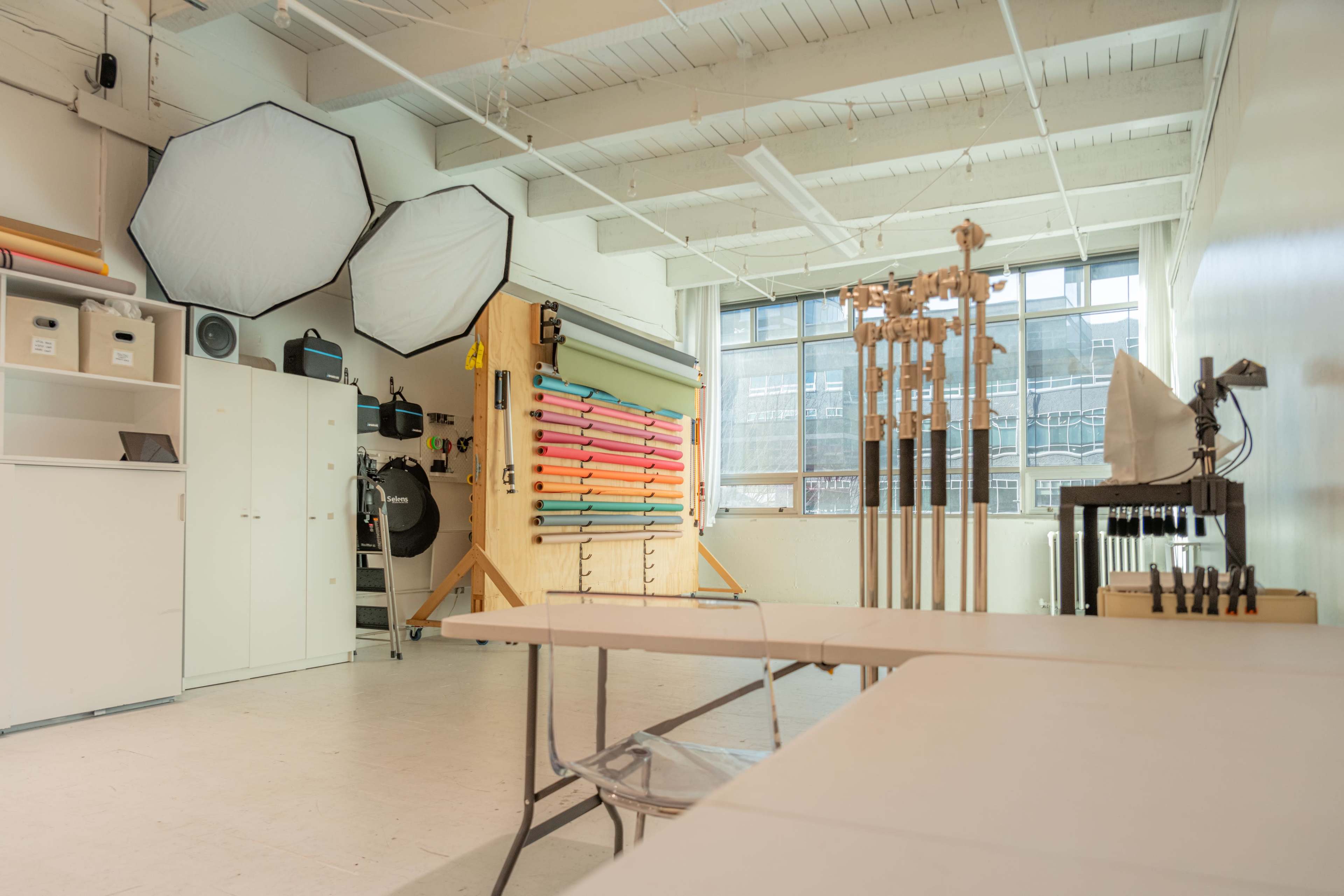 A well-lit photography studio with colorful backdrops, lighting equipment, and a large window.