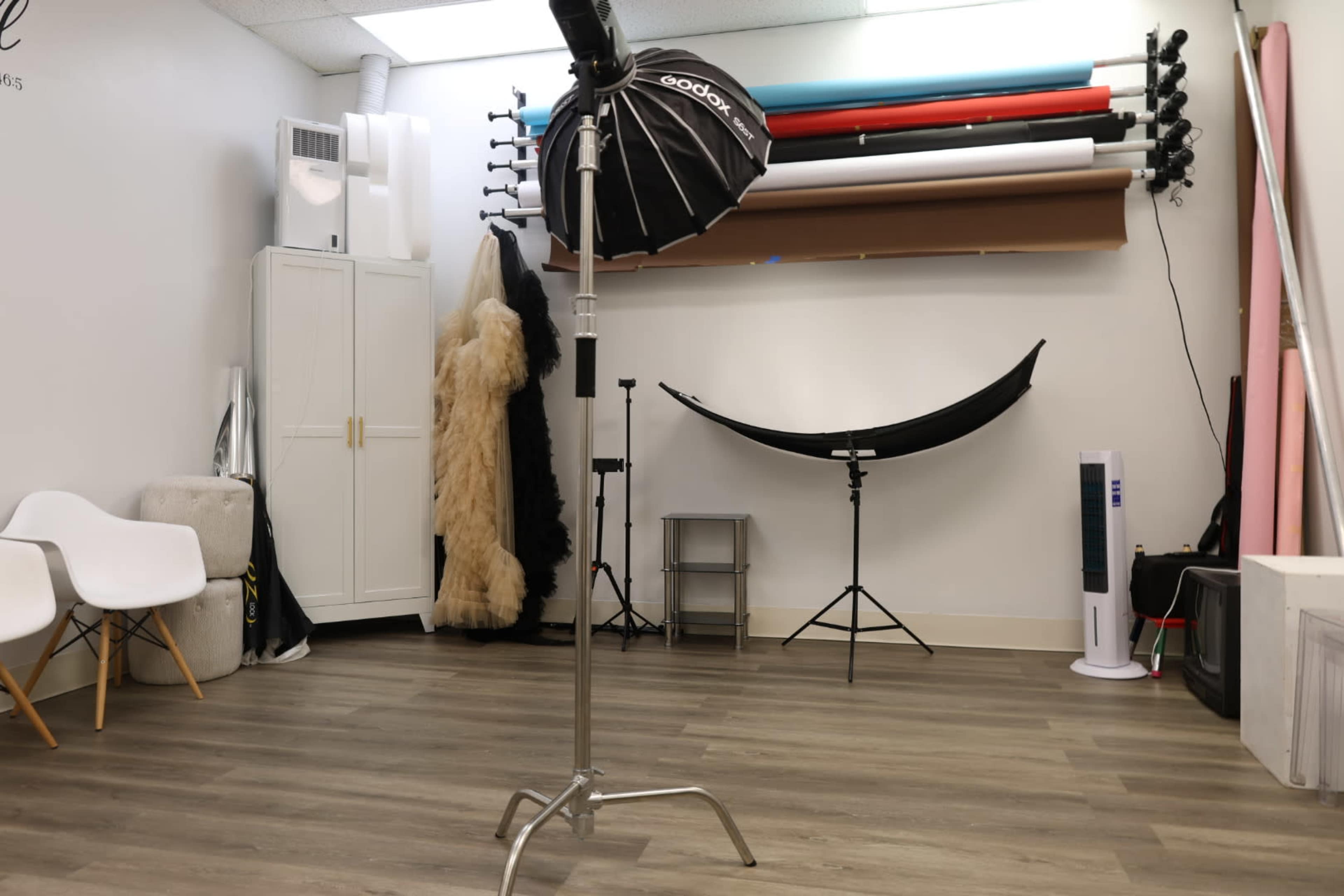 The image shows a photography studio with a background setup, lighting equipment, and various props arranged along the walls.