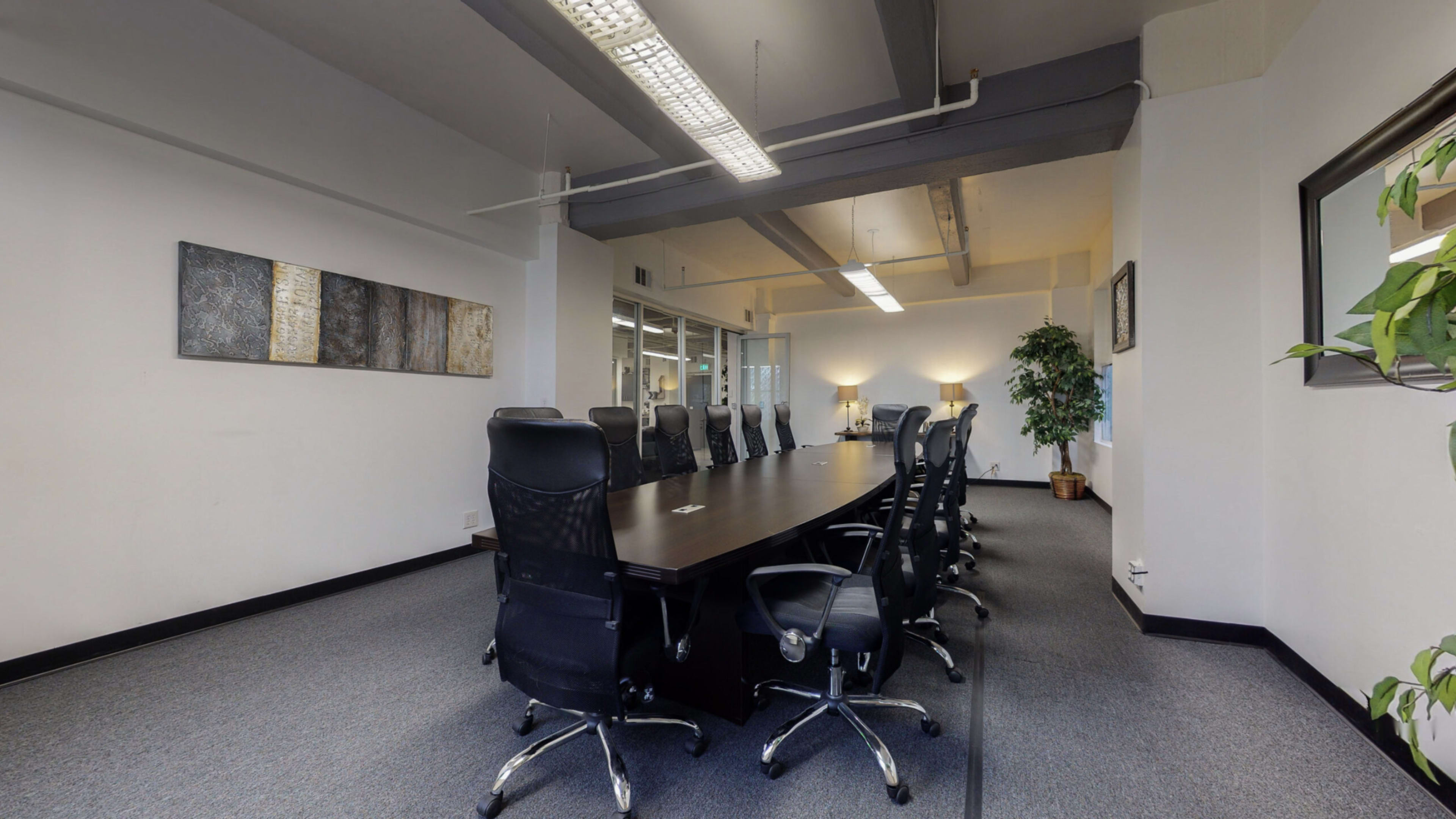 The image shows a large conference room with a long rectangular table and multiple black chairs arranged around it.