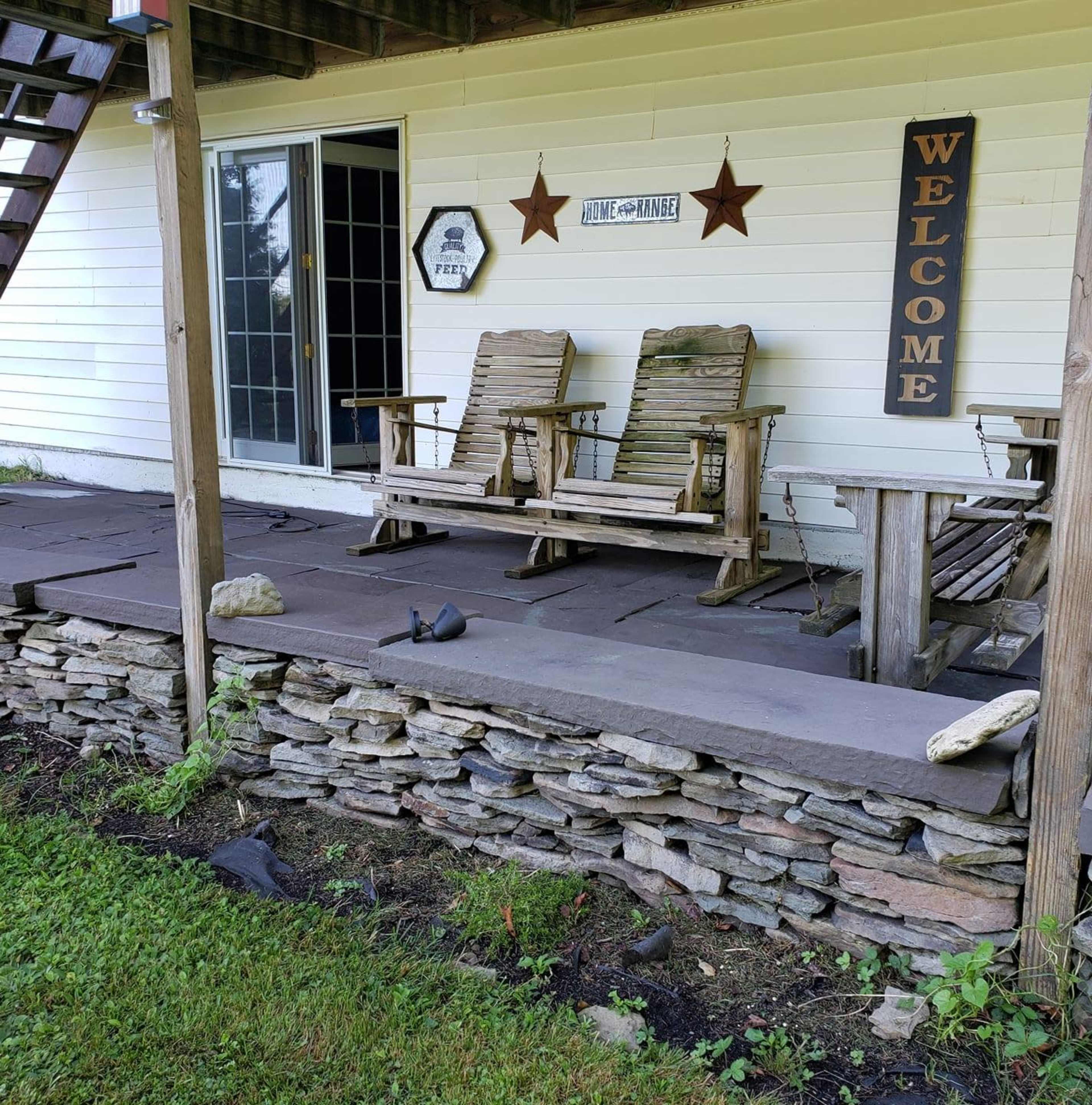 A porch area with two wooden rocking chairs, a welcome sign, and a stone wall beneath it.