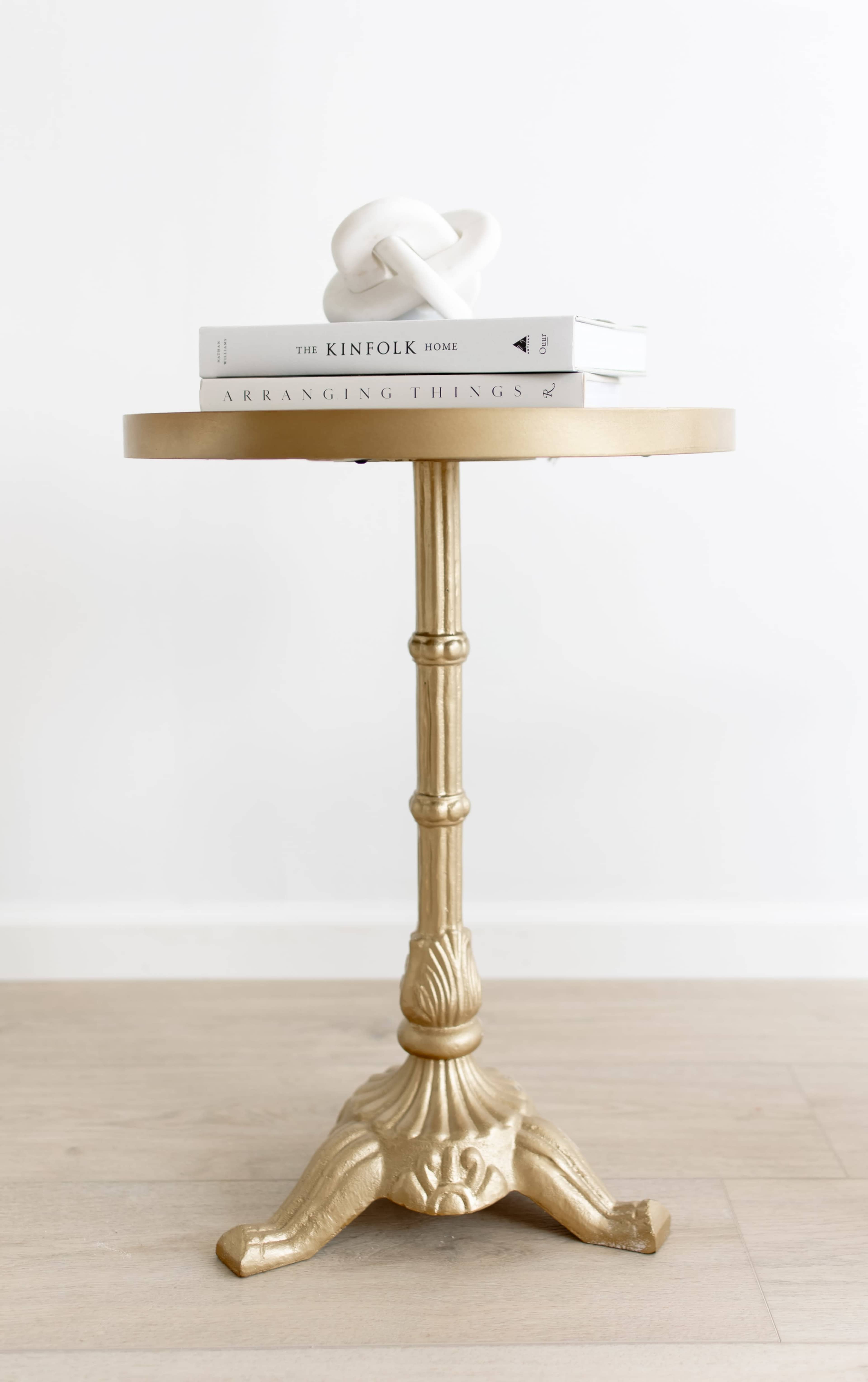 A gold side table stands on a wooden floor, topped with two stacked books and a decorative object.