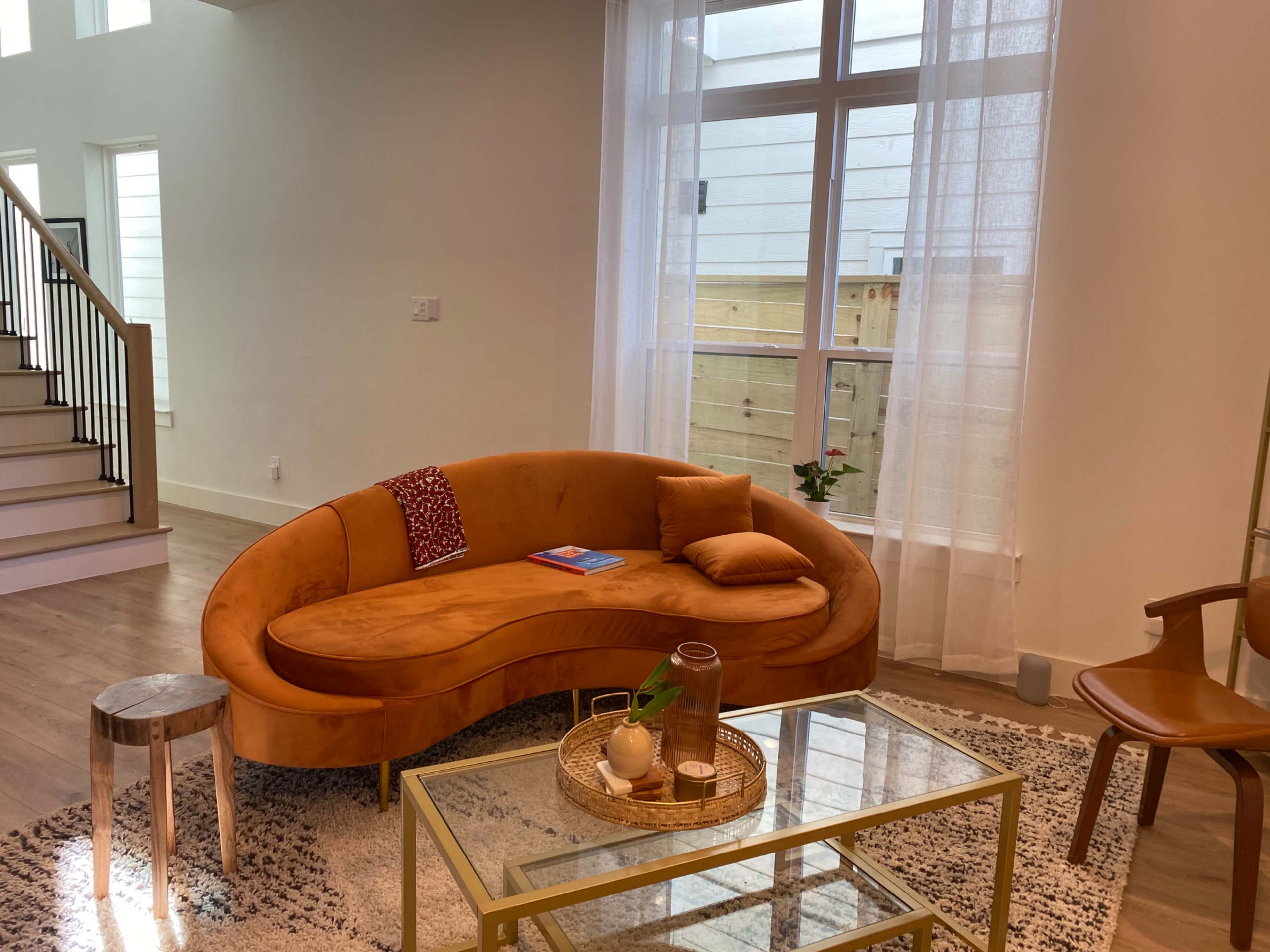 A modern living room featuring an orange curved sofa, a glass coffee table with decorative items, and a staircase in the background.