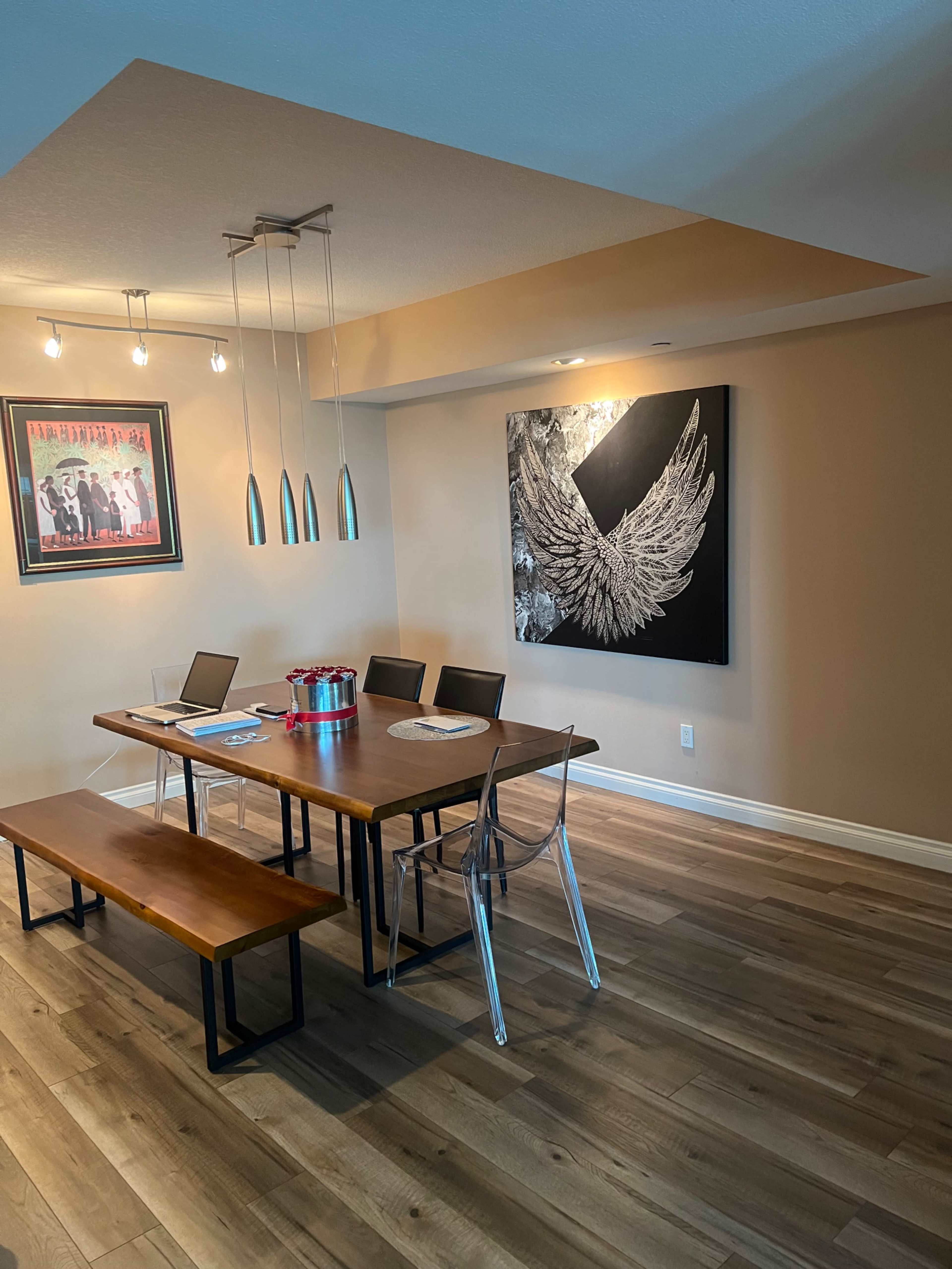 A dining area features a rectangular wooden table surrounded by chairs, a bench, and a large wall art piece of wings.