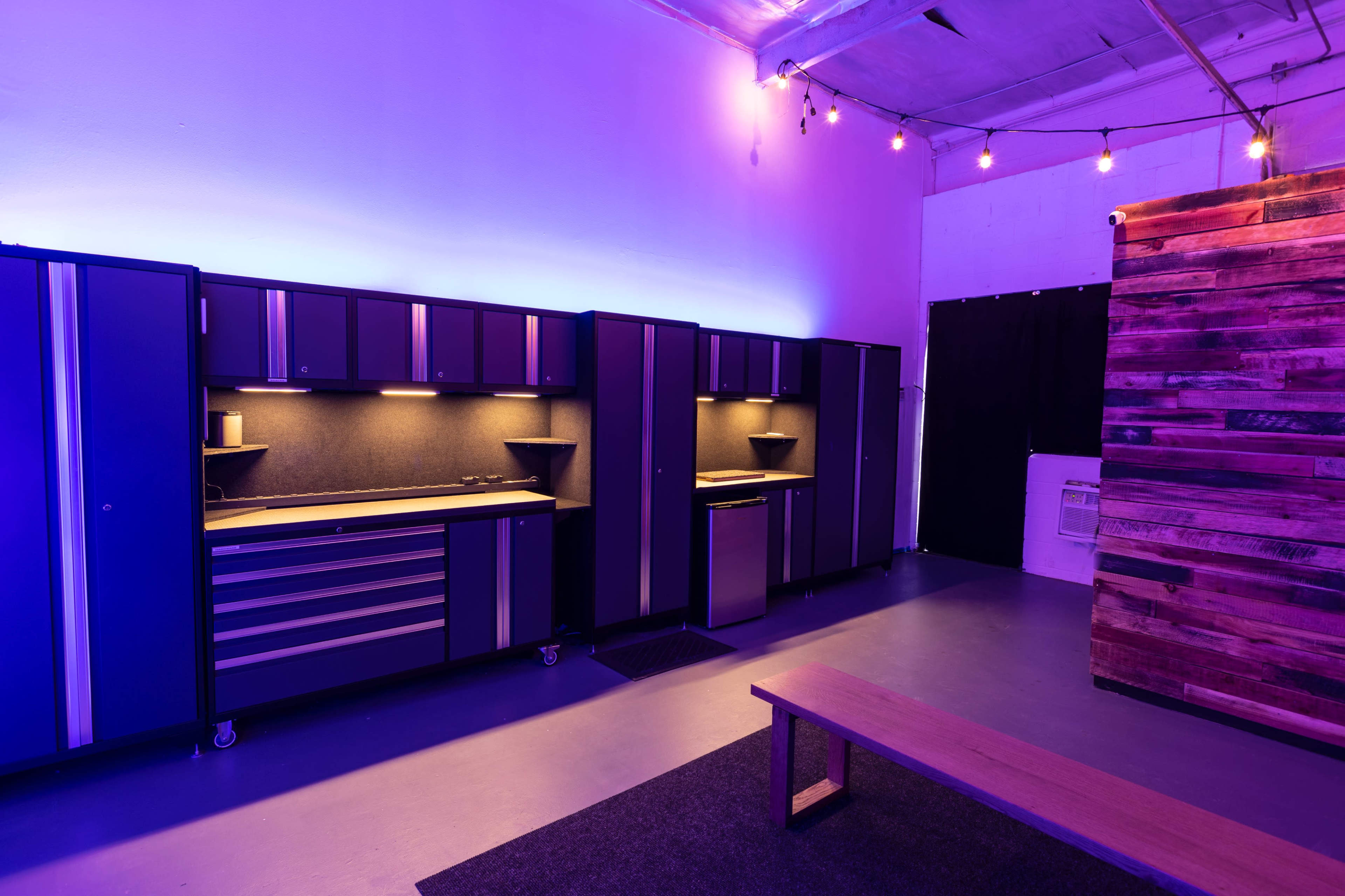 A modern garage space with dark cabinetry and overhead lighting, featuring a wooden bench and a wall made of wood planks.