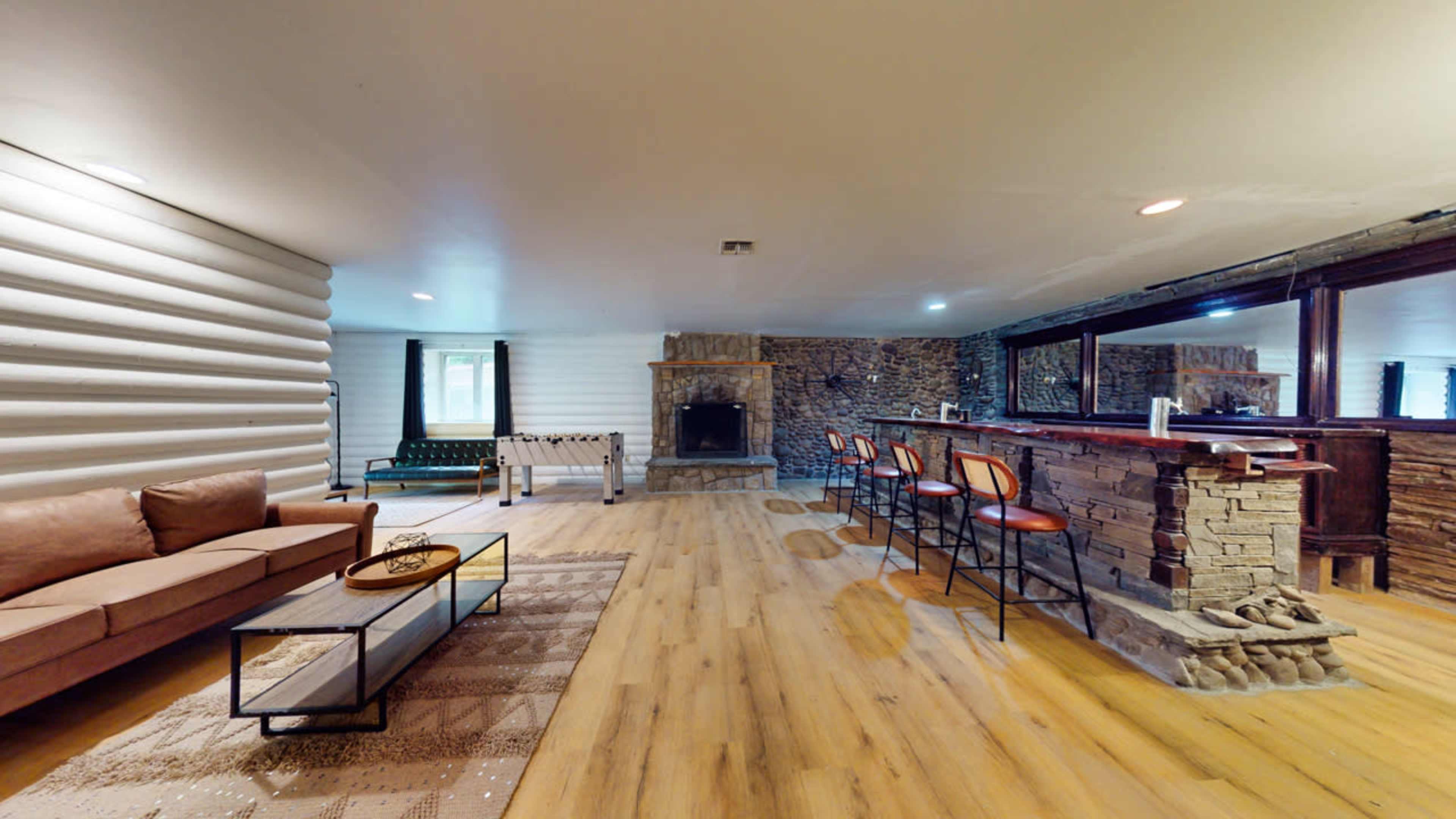 A spacious living area with a brown sofa, a coffee table, a pool table, a stone fireplace, and a bar with high stools.