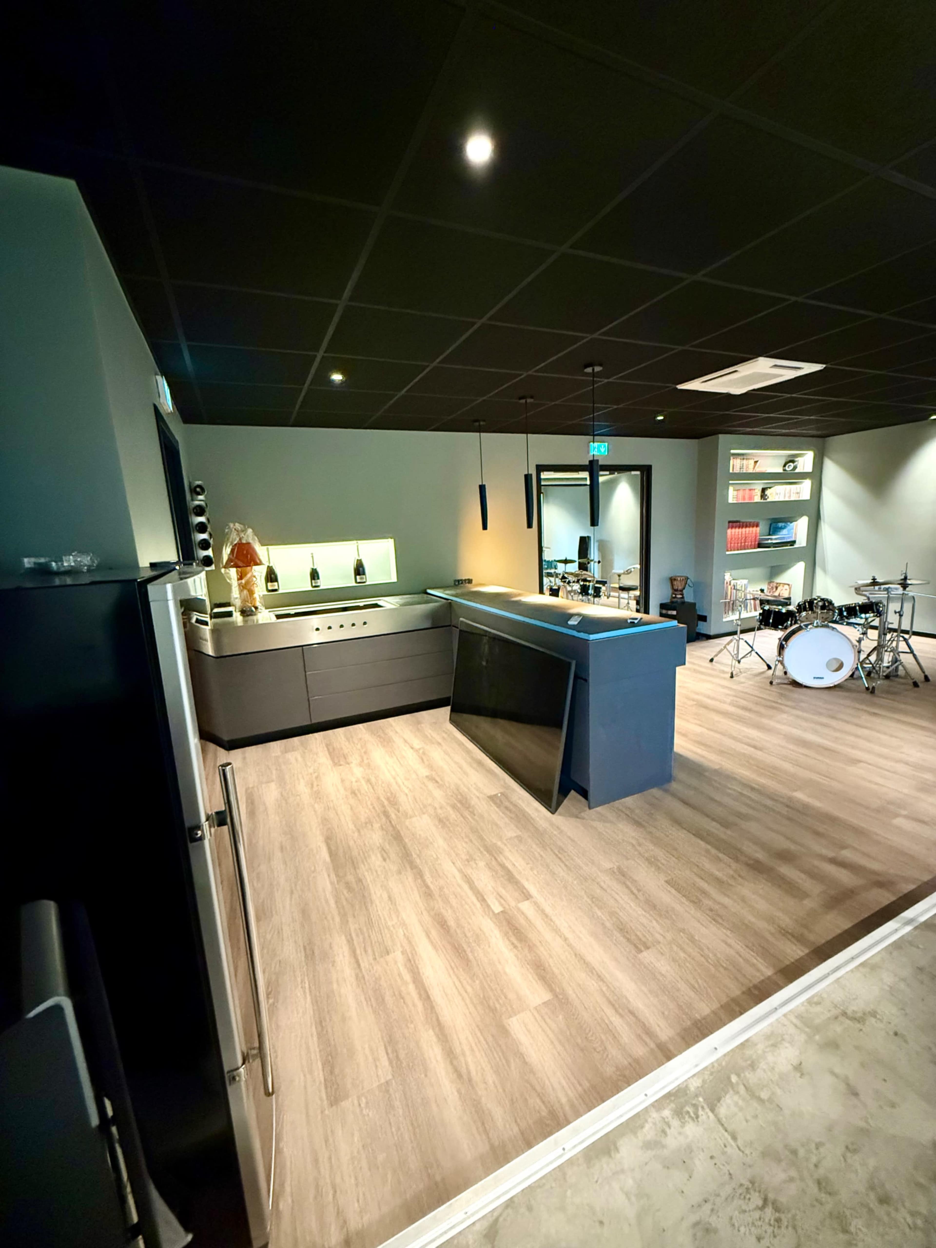 The image shows a modern, open kitchen area with a bar and a small drum set in the corner of a stylish room.