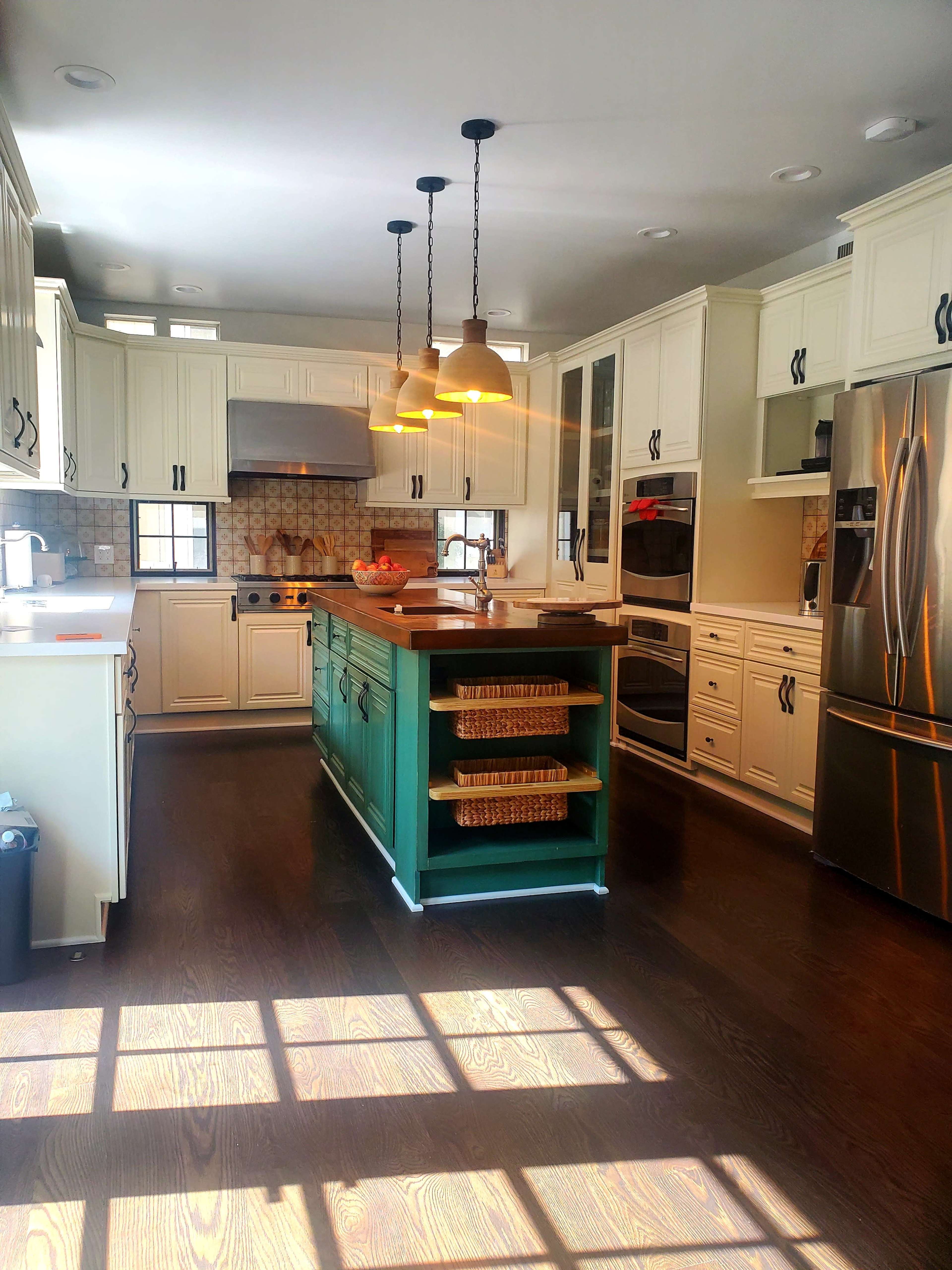 The kitchen features white cabinets, a green island with storage baskets, stainless steel appliances, and pendant lighting.