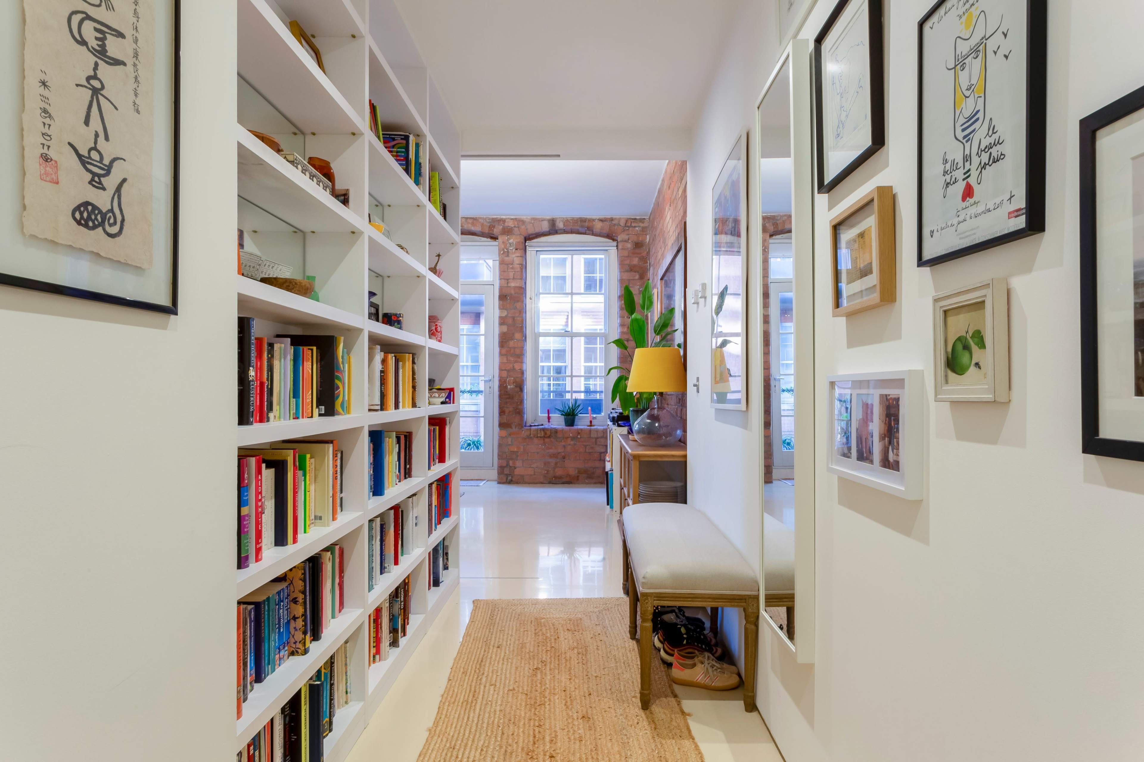 A well-lit hallway lined with shelves of books, a bench, and a wall adorned with framed art.