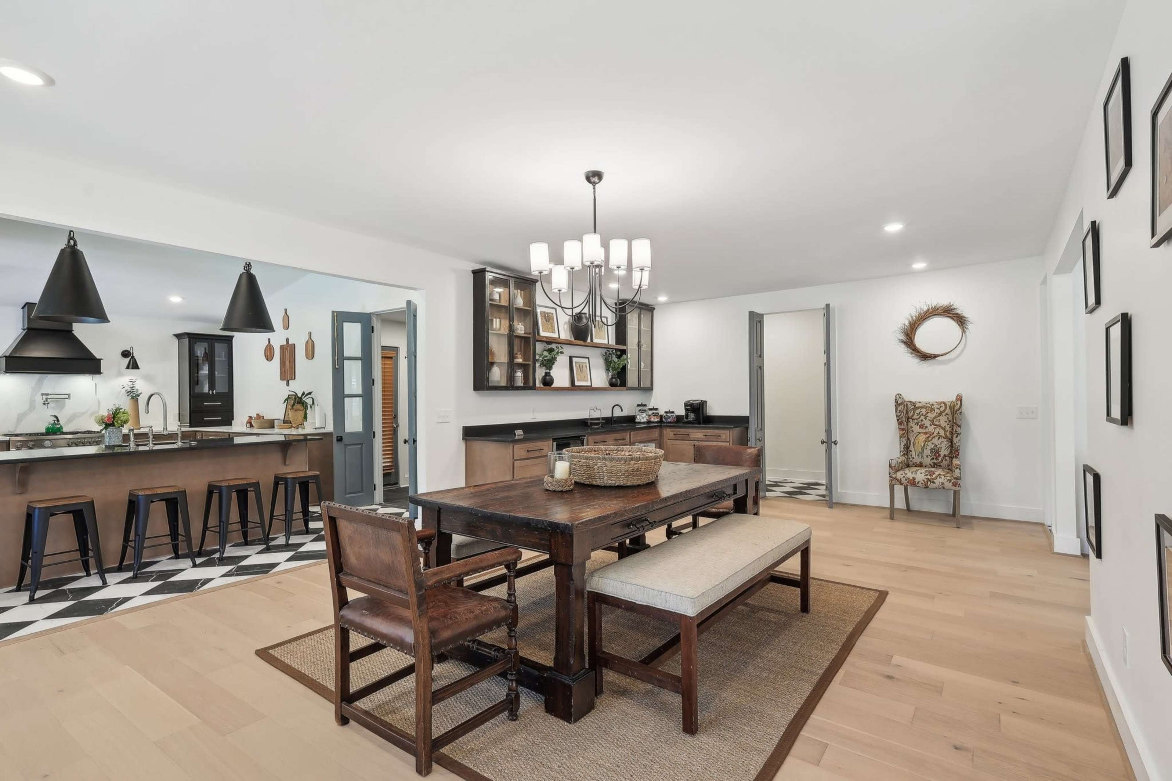 A modern kitchen and dining area featuring a wooden dining table with benches, black cabinets, and checkerboard flooring.