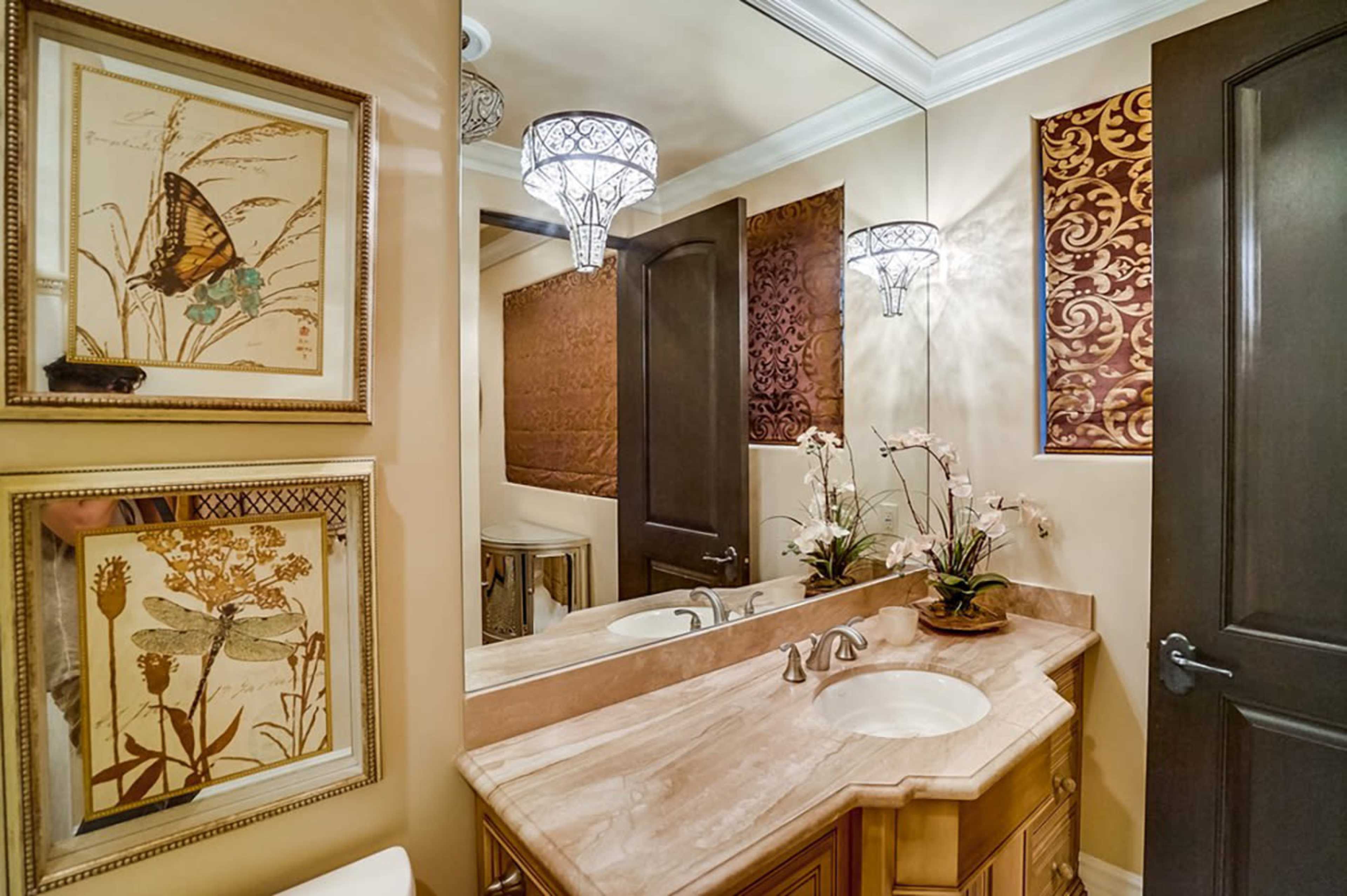 A bathroom featuring a marble countertop with double sinks, decorative wall art of butterflies and flowers, and two pendant lights hanging from the ceiling.
