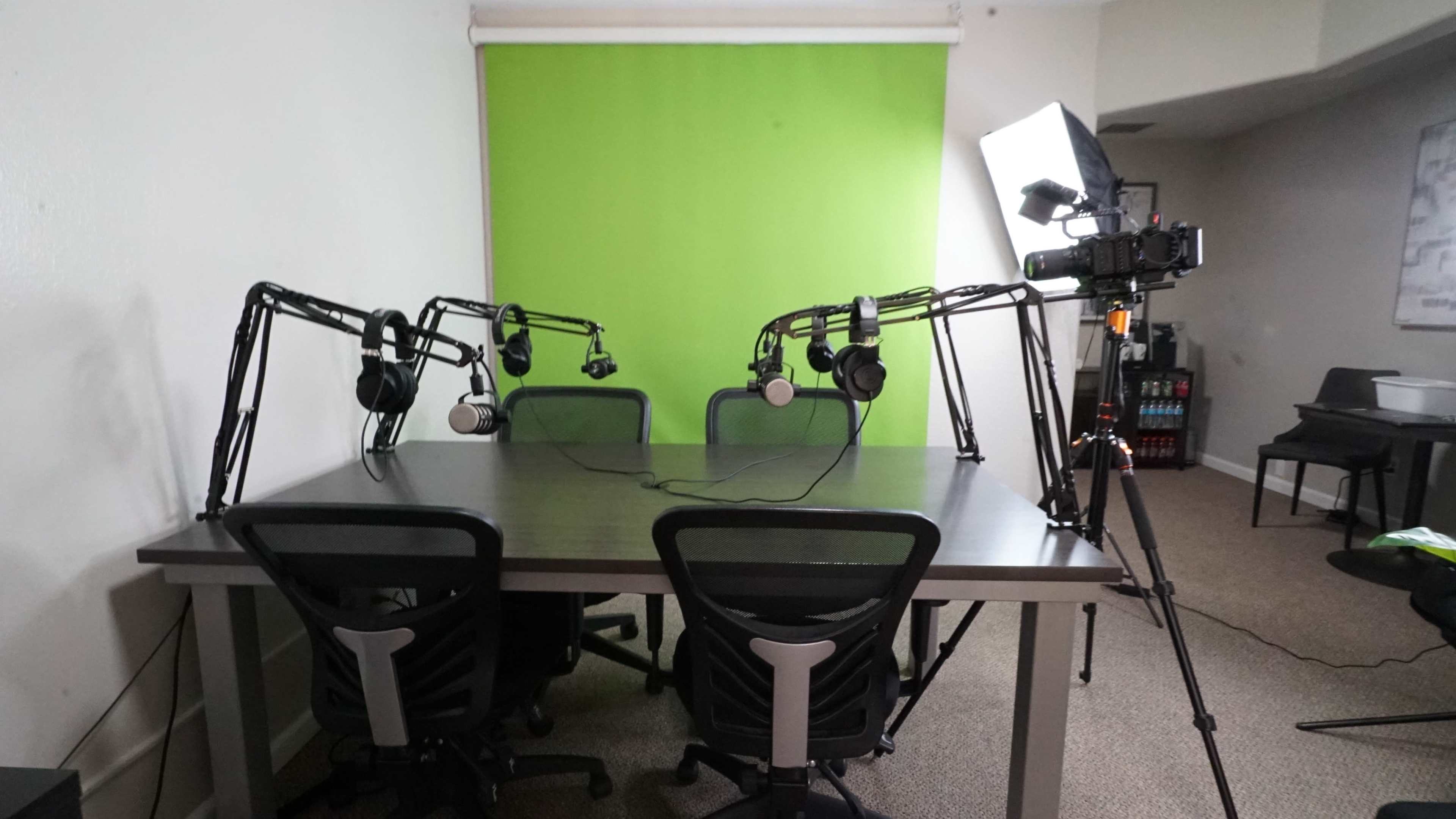 A conference room with a table, four chairs, and equipment for recording, including microphones and a camera positioned on a tripod.