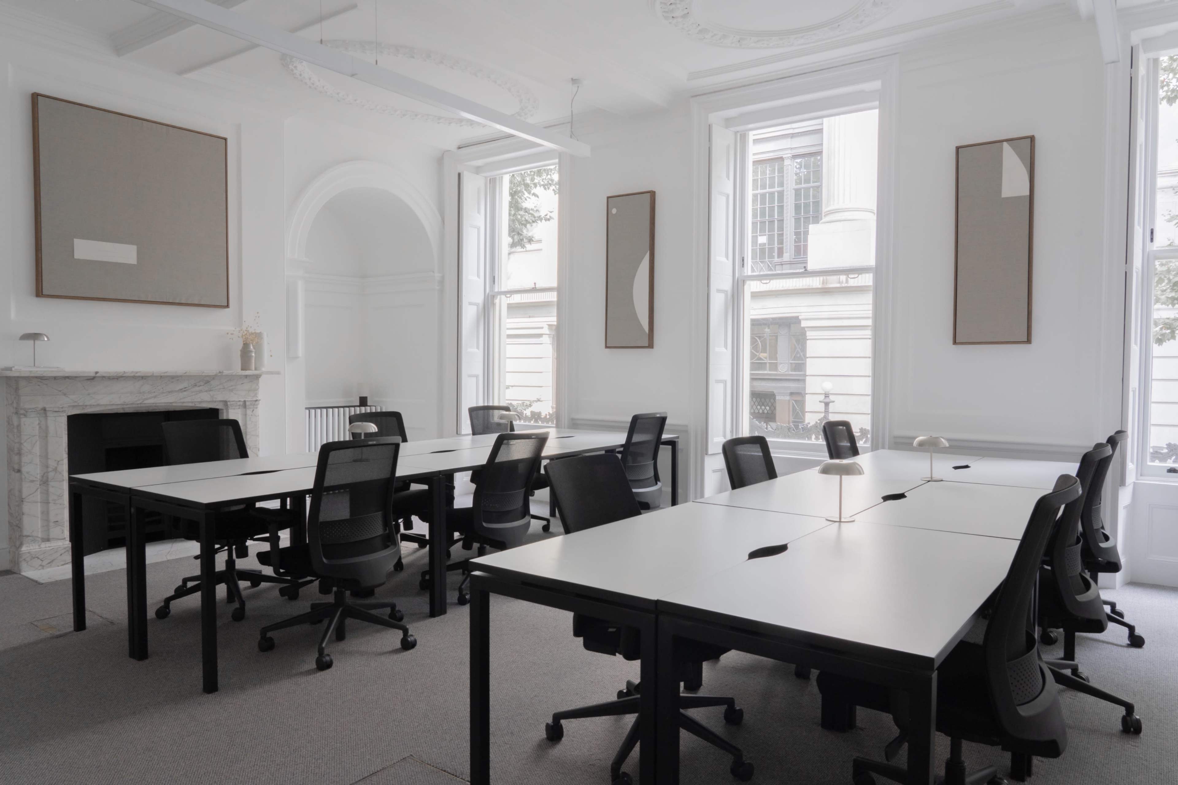 A modern meeting room features several rectangular tables with ergonomic chairs arranged in a spacious layout, accented by minimalistic artwork on the walls.