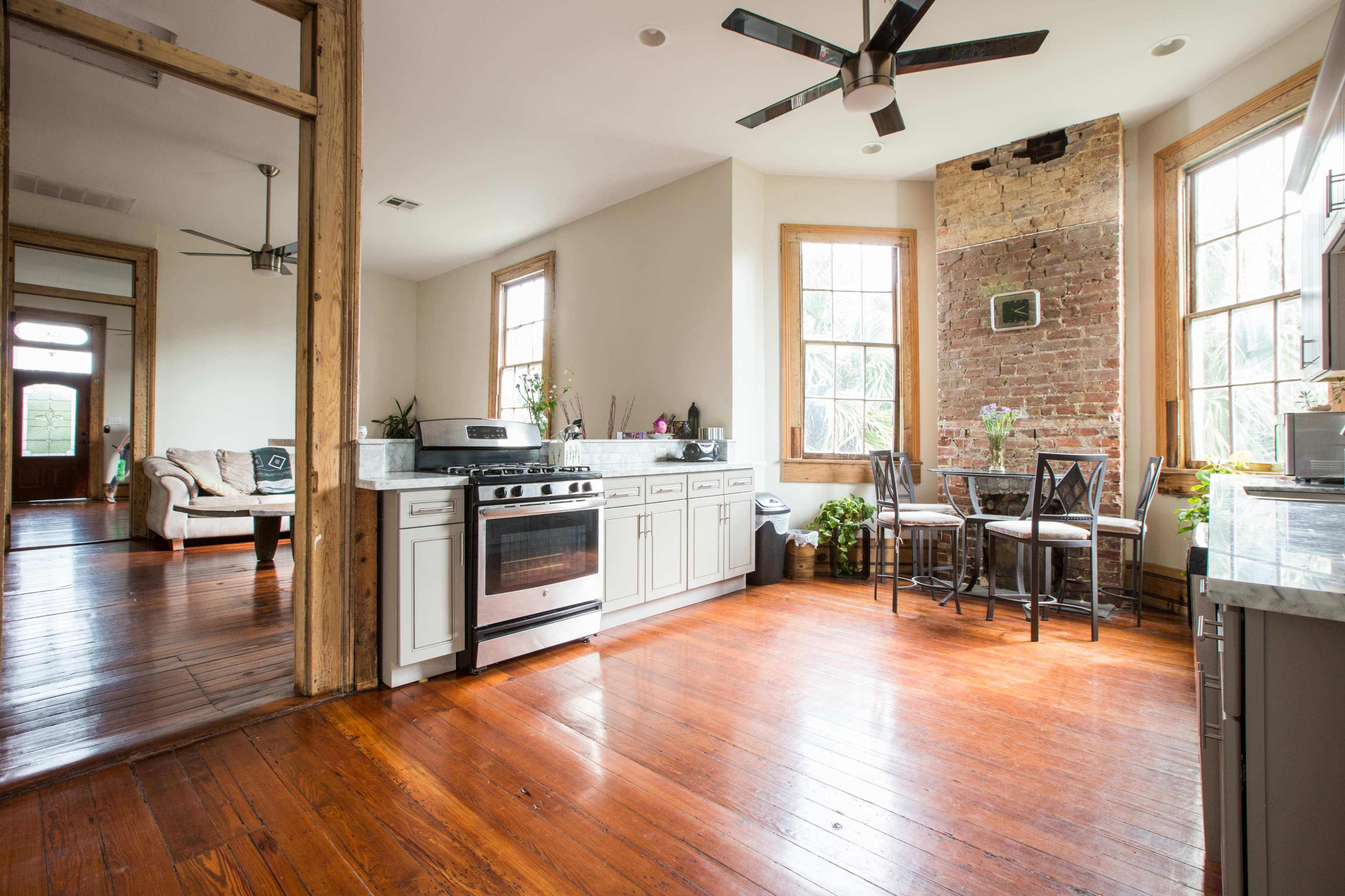 A kitchen with a stove, cabinets, and a dining area featuring a table and chairs, adjacent to a living space with wooden floors and large windows.