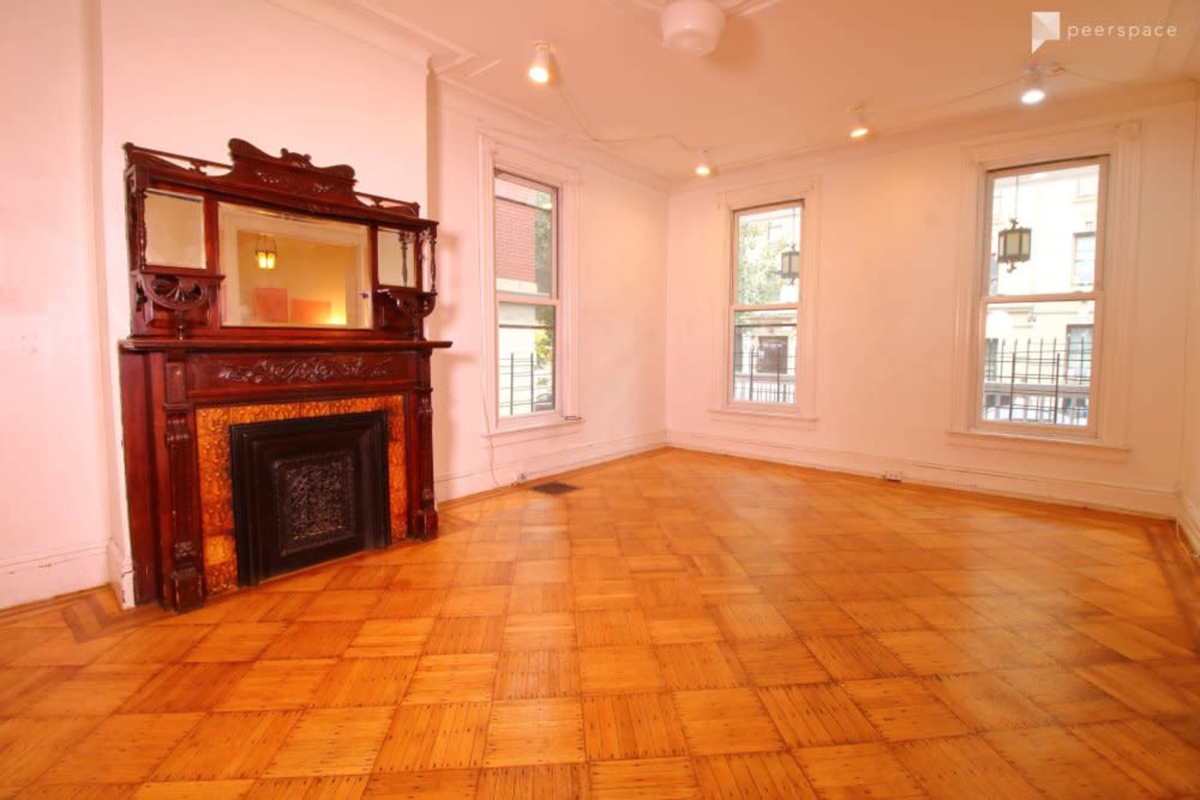 A brightly lit room with polished parquet flooring, featuring a wooden fireplace mantel and a mirror above it.