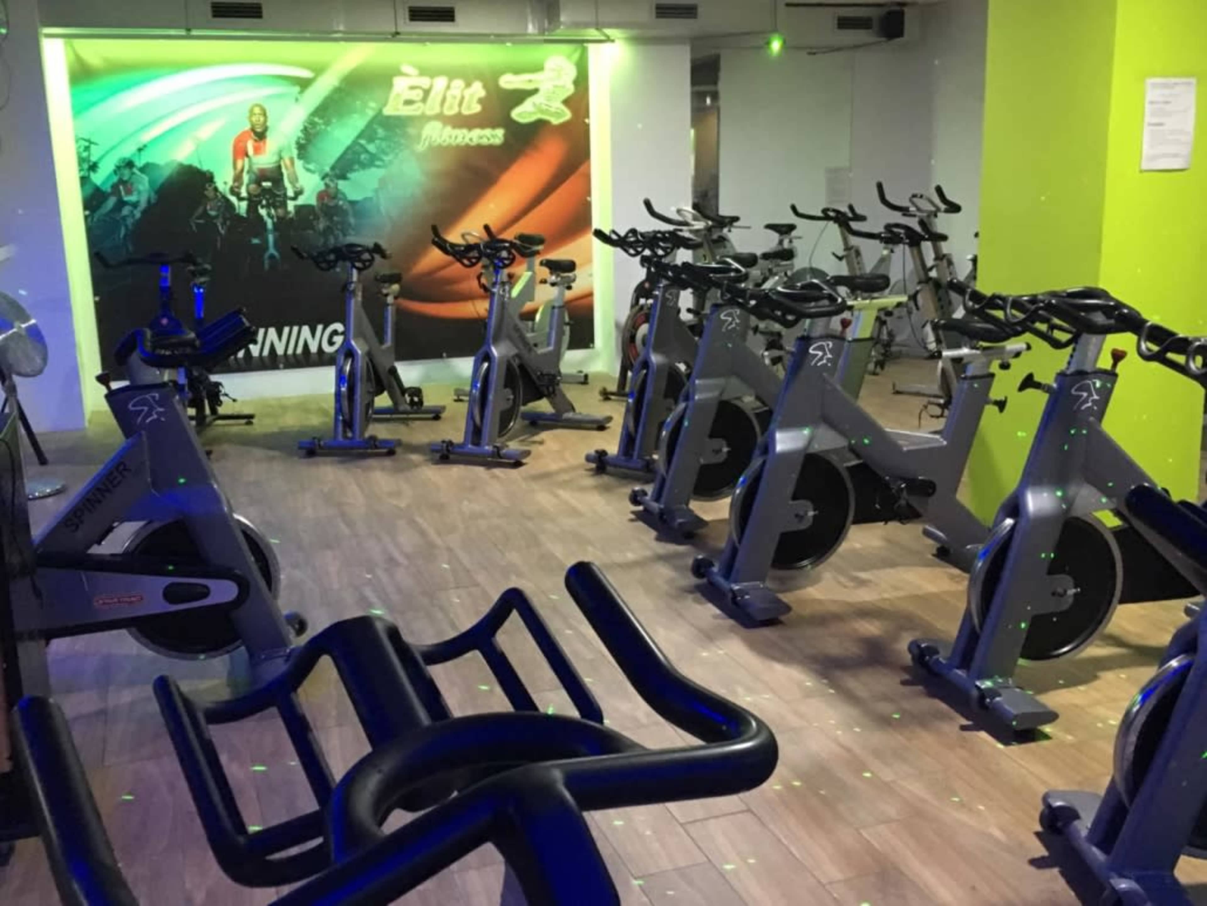 The image shows a fitness studio filled with stationary exercise bikes, featuring a colorful mural on the wall and dim lighting with green dots.