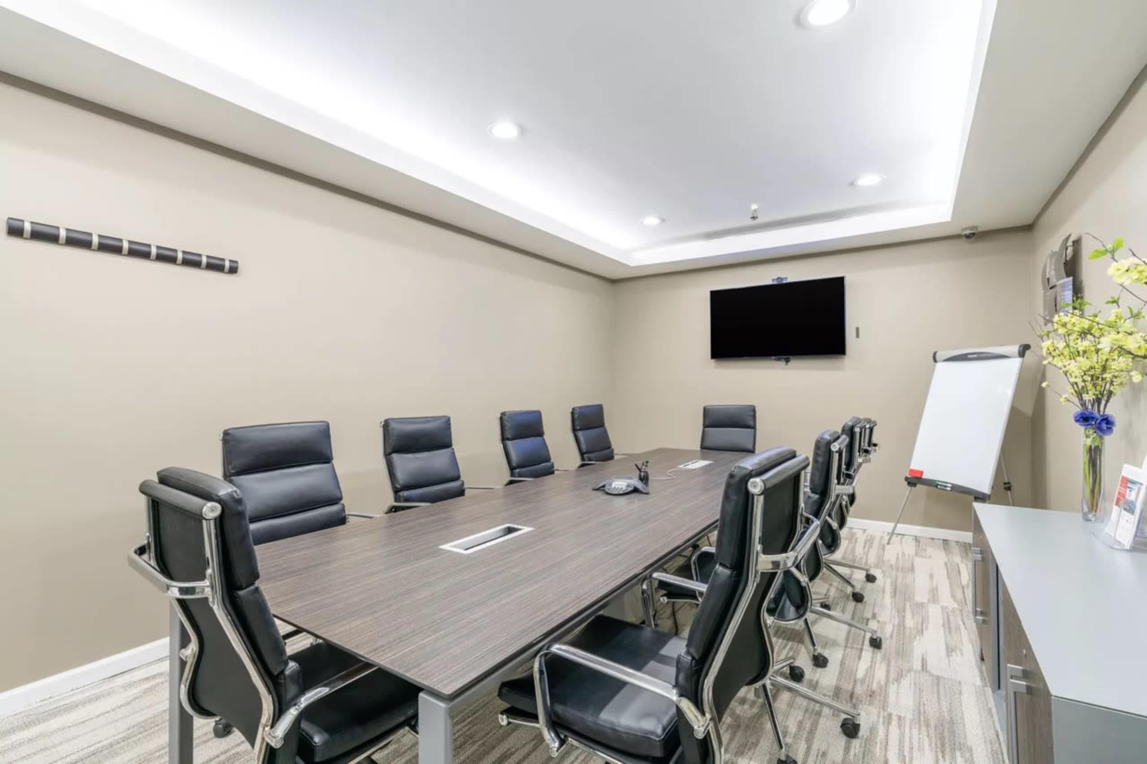 A modern conference room with a long table, black leather chairs, and a wall-mounted screen.