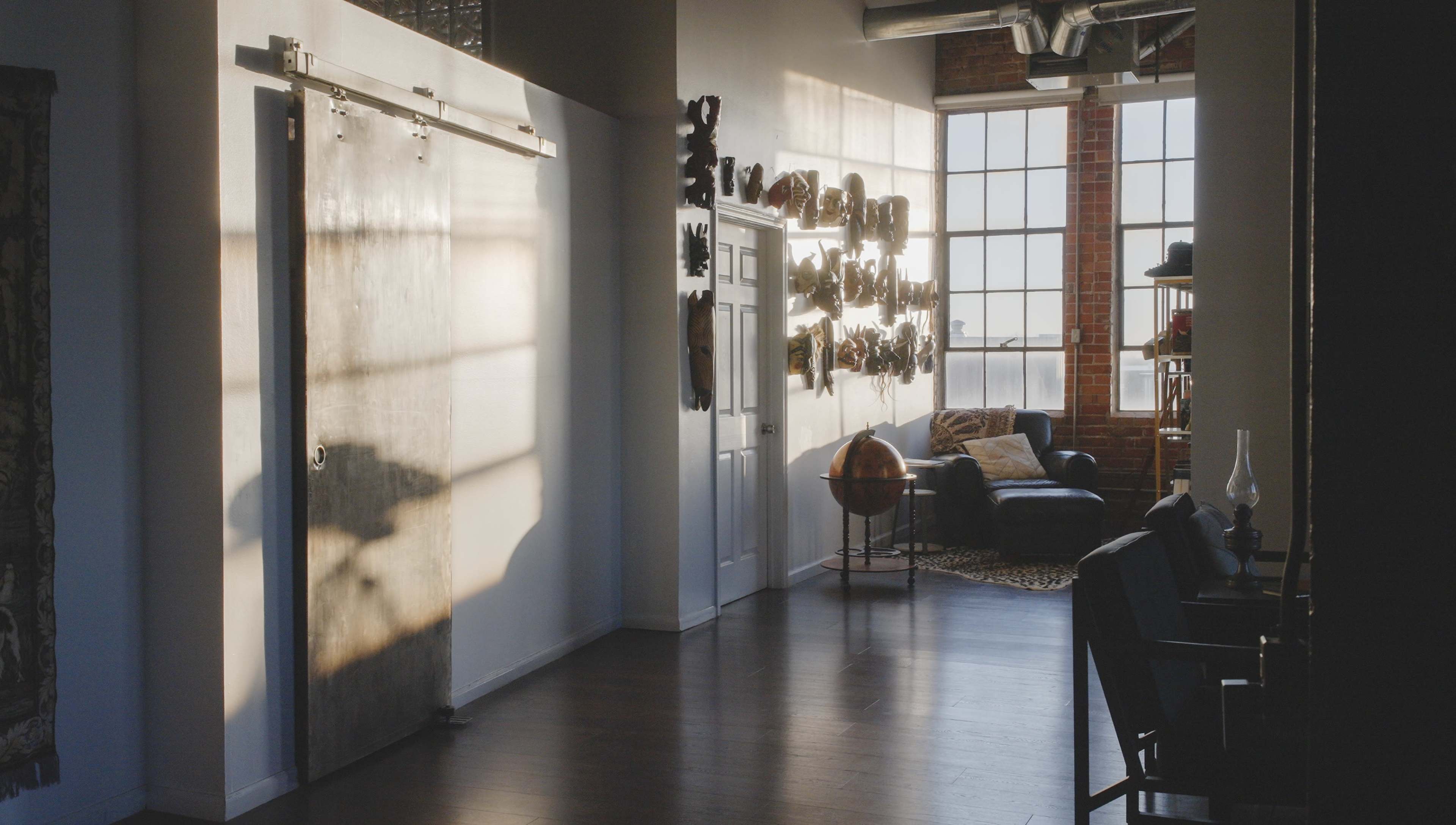 The image shows a bright, spacious interior with a sliding barn door, brick walls, large windows, and a modern seating area.