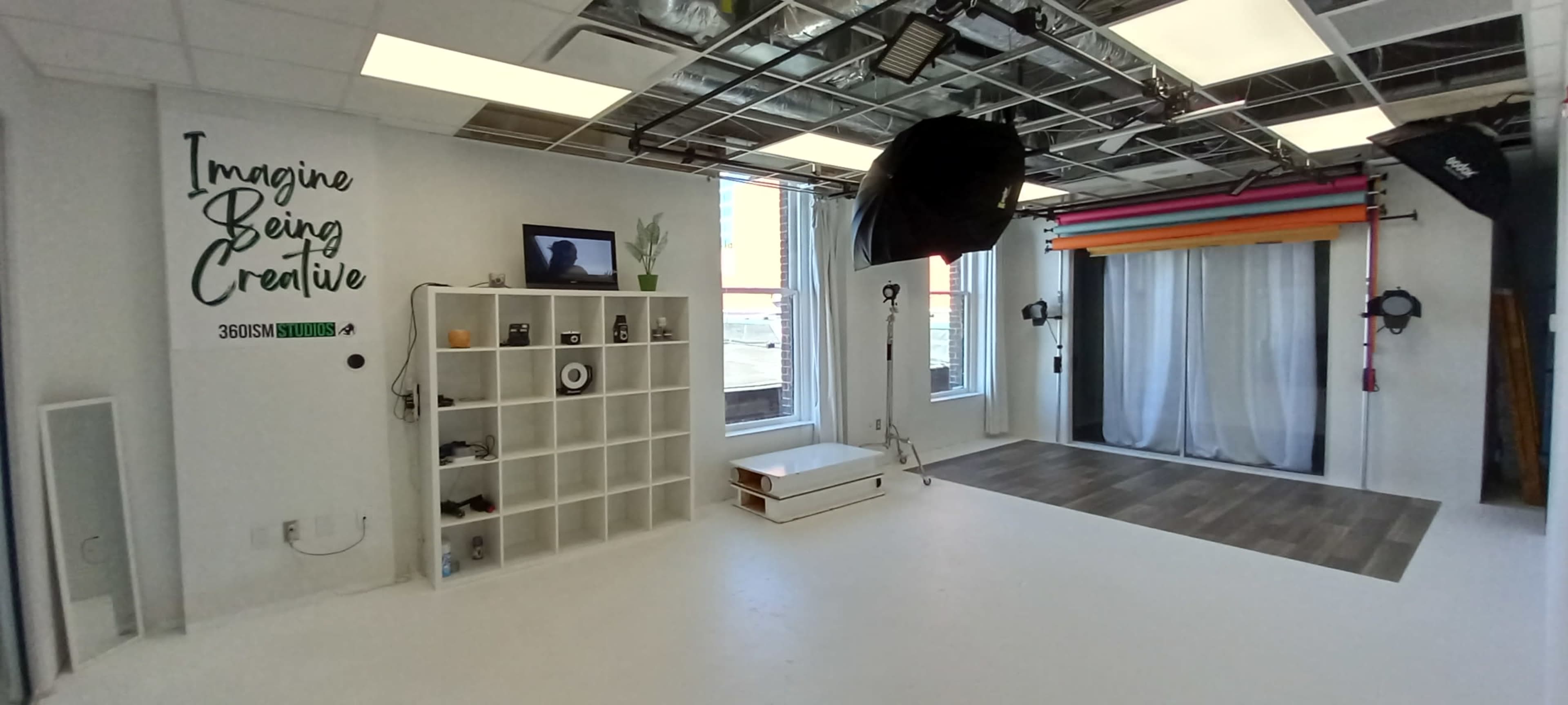 A creative studio space with white walls, a grid ceiling, and a backdrop area featuring colorful drapes.