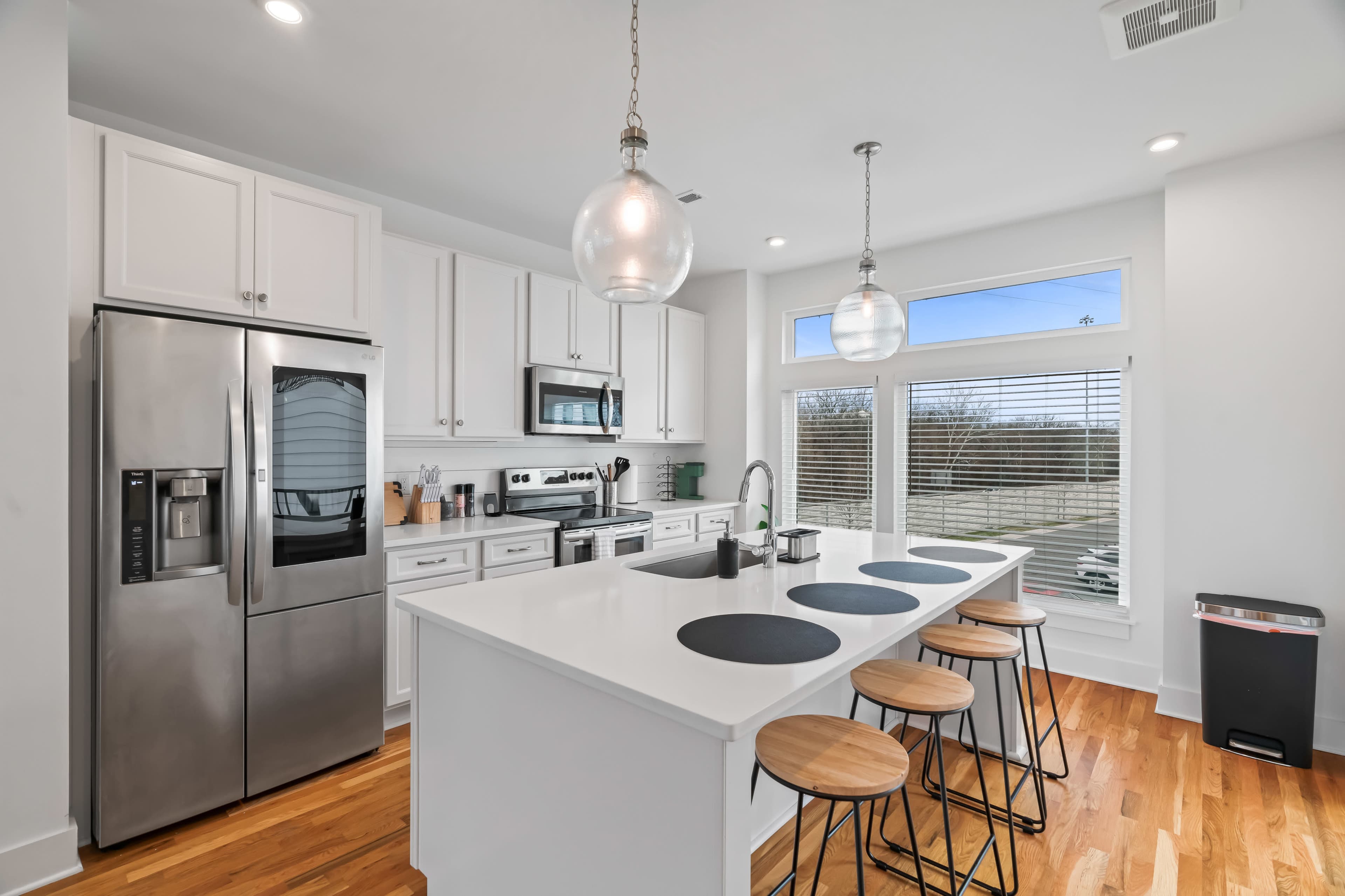 A modern kitchen with white cabinets, stainless steel appliances, and a breakfast bar featuring four wooden stools.