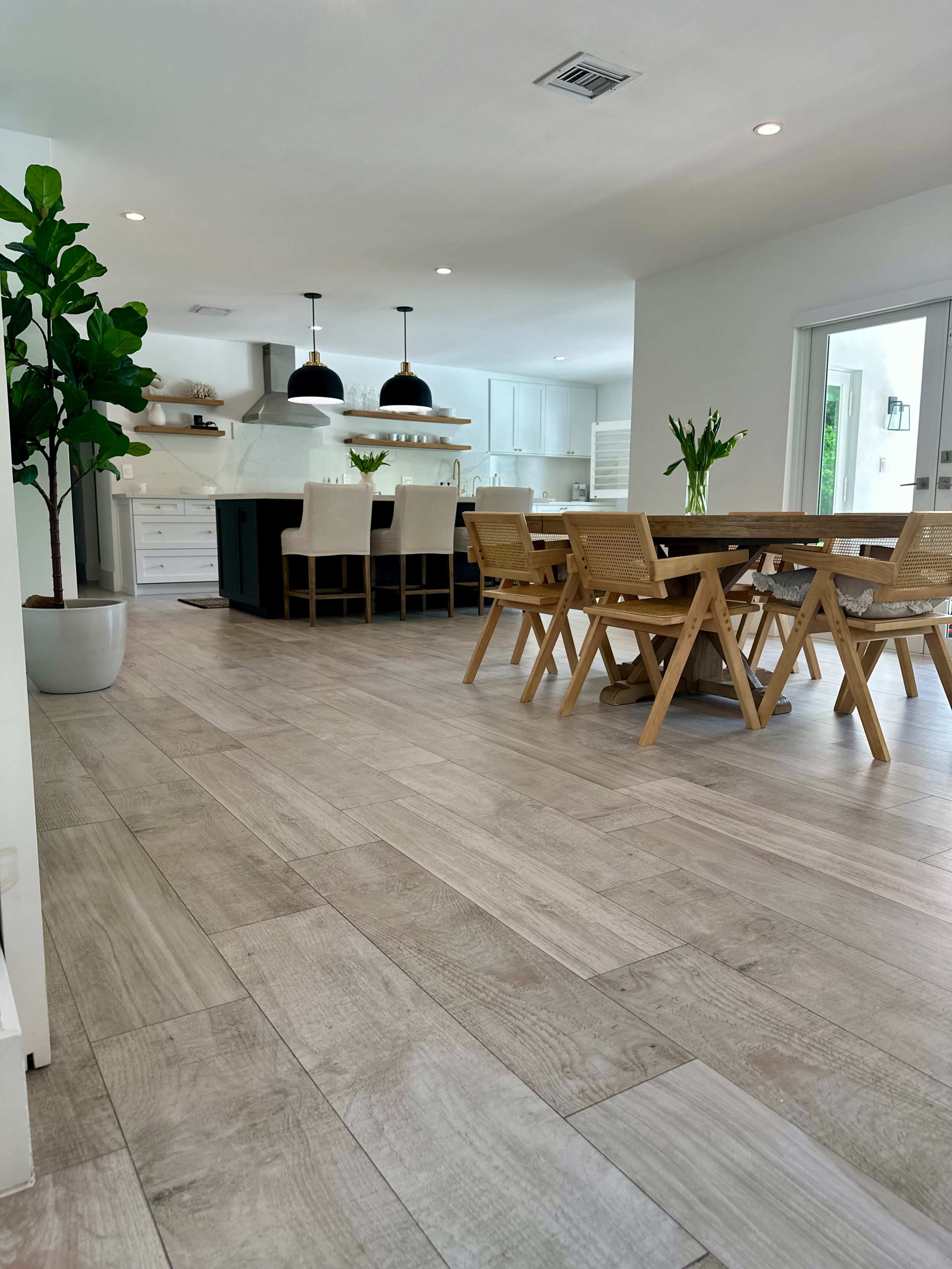 The image shows a modern kitchen and dining area with wooden flooring, a large dining table, and a kitchen island with pendant lighting.