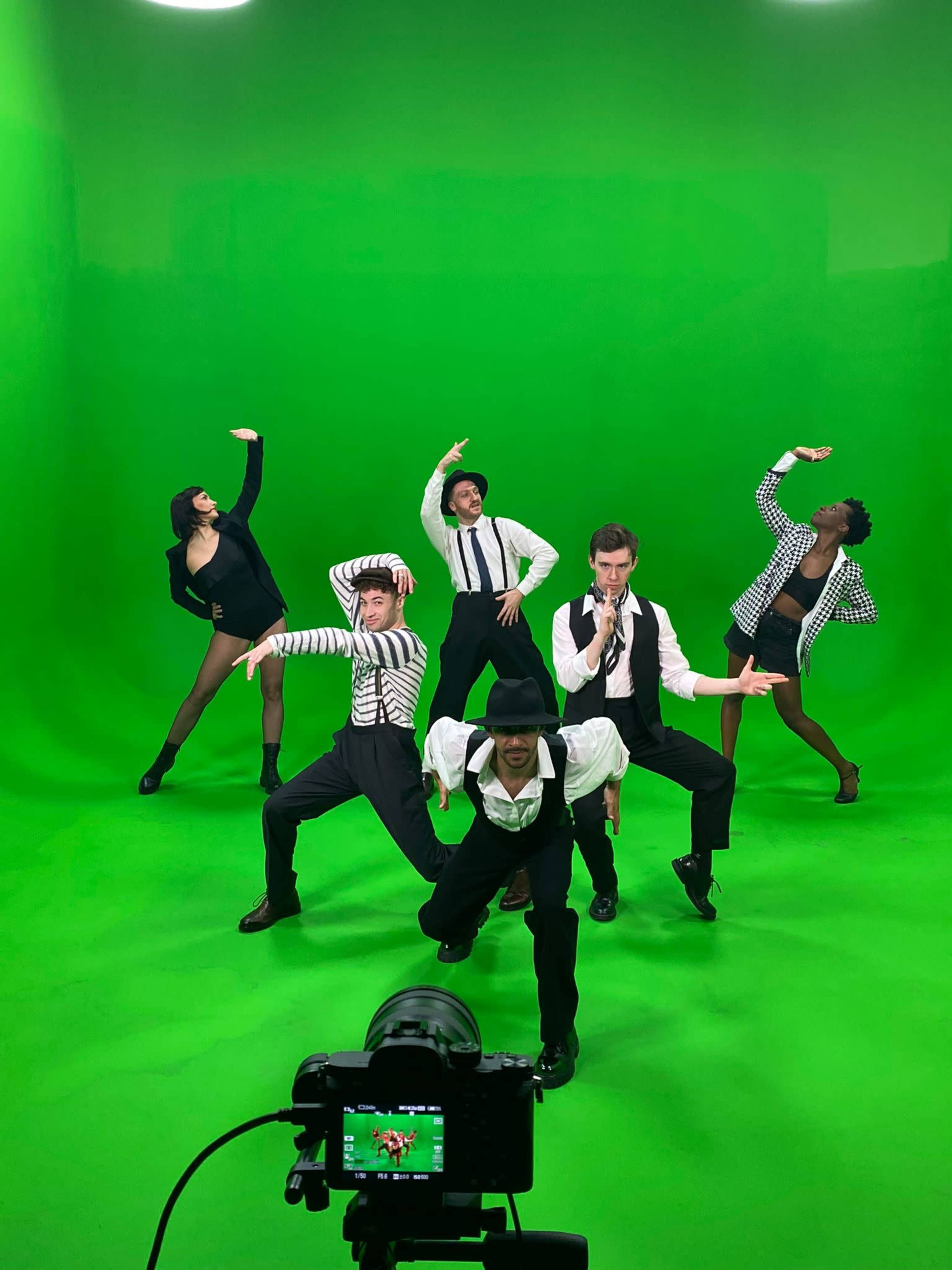 A group of six performers poses dramatically on a green screen backdrop, showcasing a variety of styles and expressions.