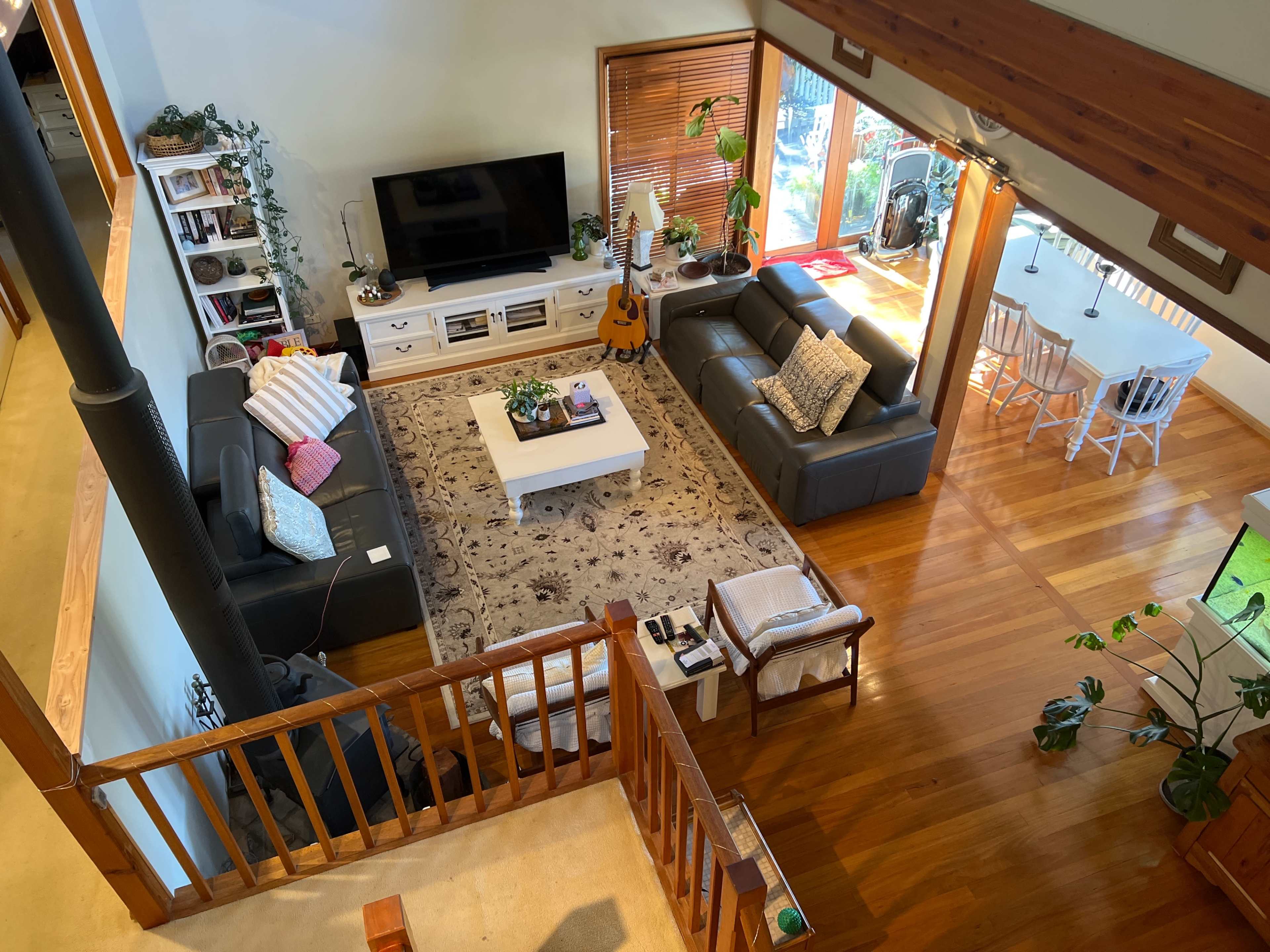A spacious living room with two black sofas, a large area rug, a coffee table, a television unit, and a dining area with white chairs in a well-lit setting.