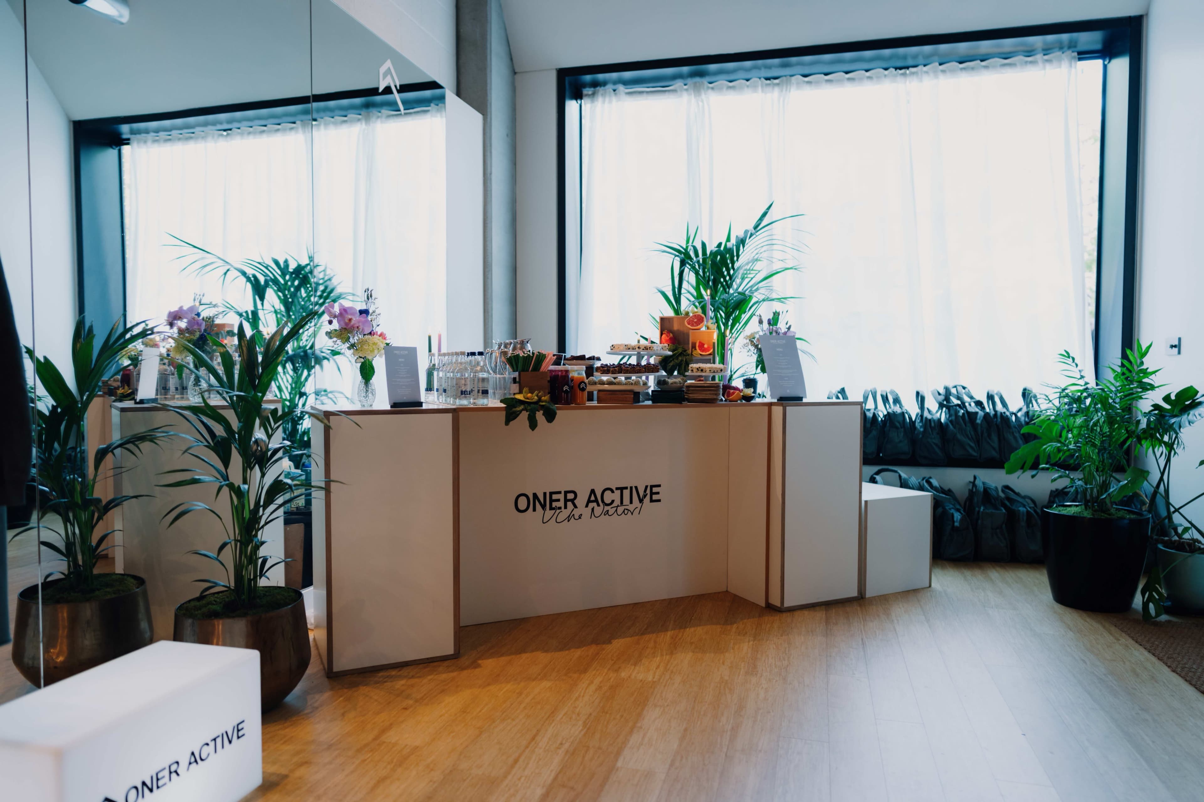 The image shows a well-lit reception area with a modern white counter adorned with plants and promotional materials.