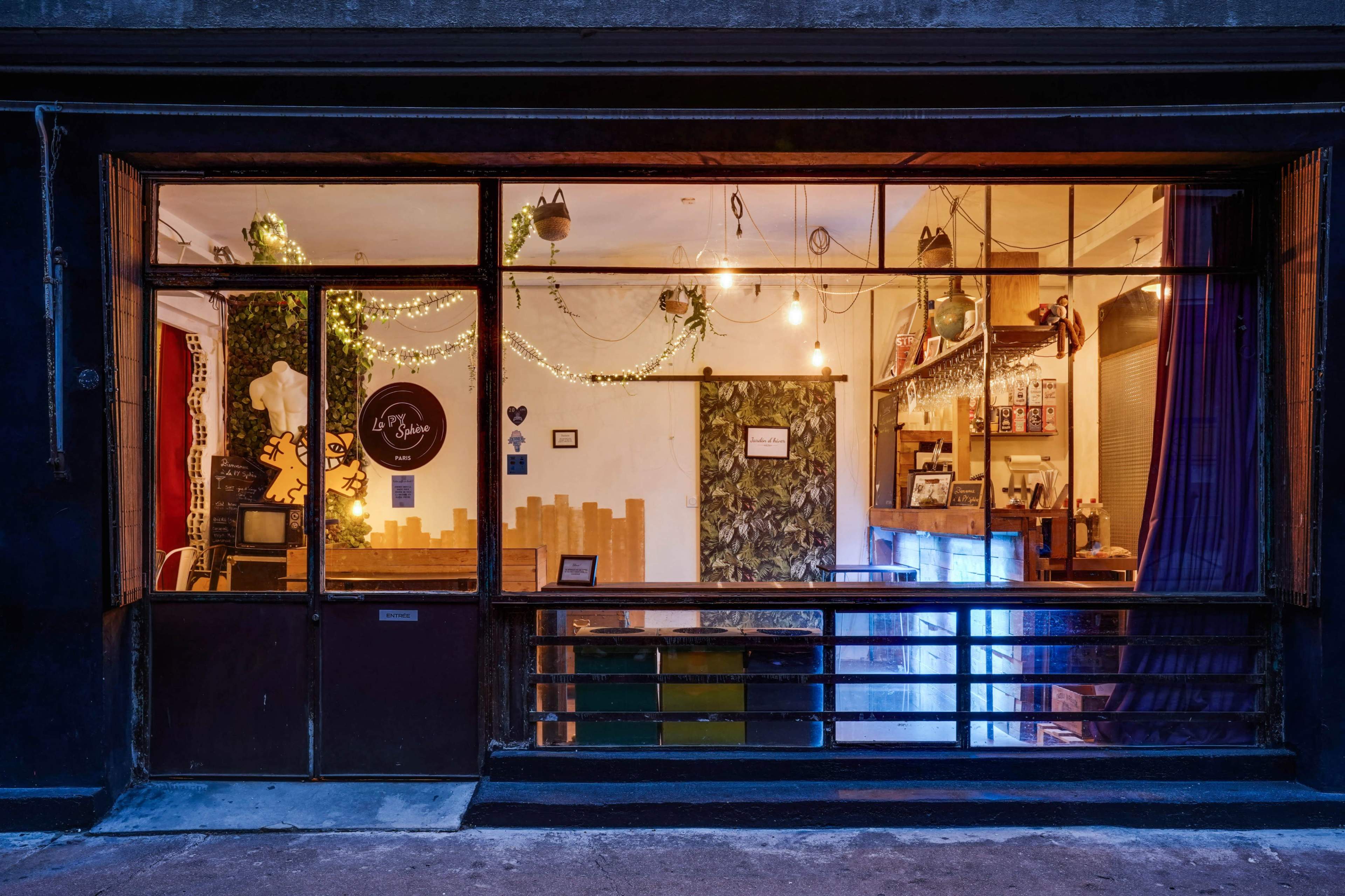 A shop window displays a cozy interior adorned with plants, lights, and wooden decor.