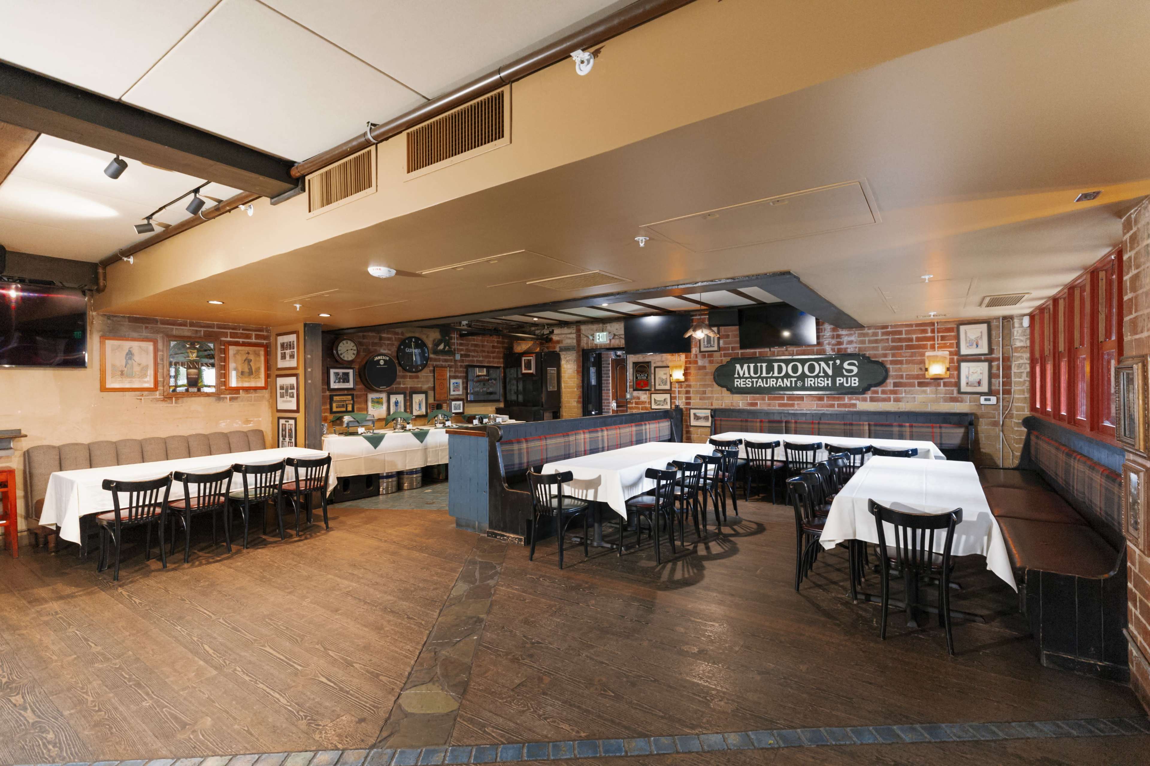 The image shows the interior of Muldoon's Restaurant and Irish Pub, featuring wooden flooring, a mix of table settings with white tablecloths, and exposed brick walls decorated with artwork.