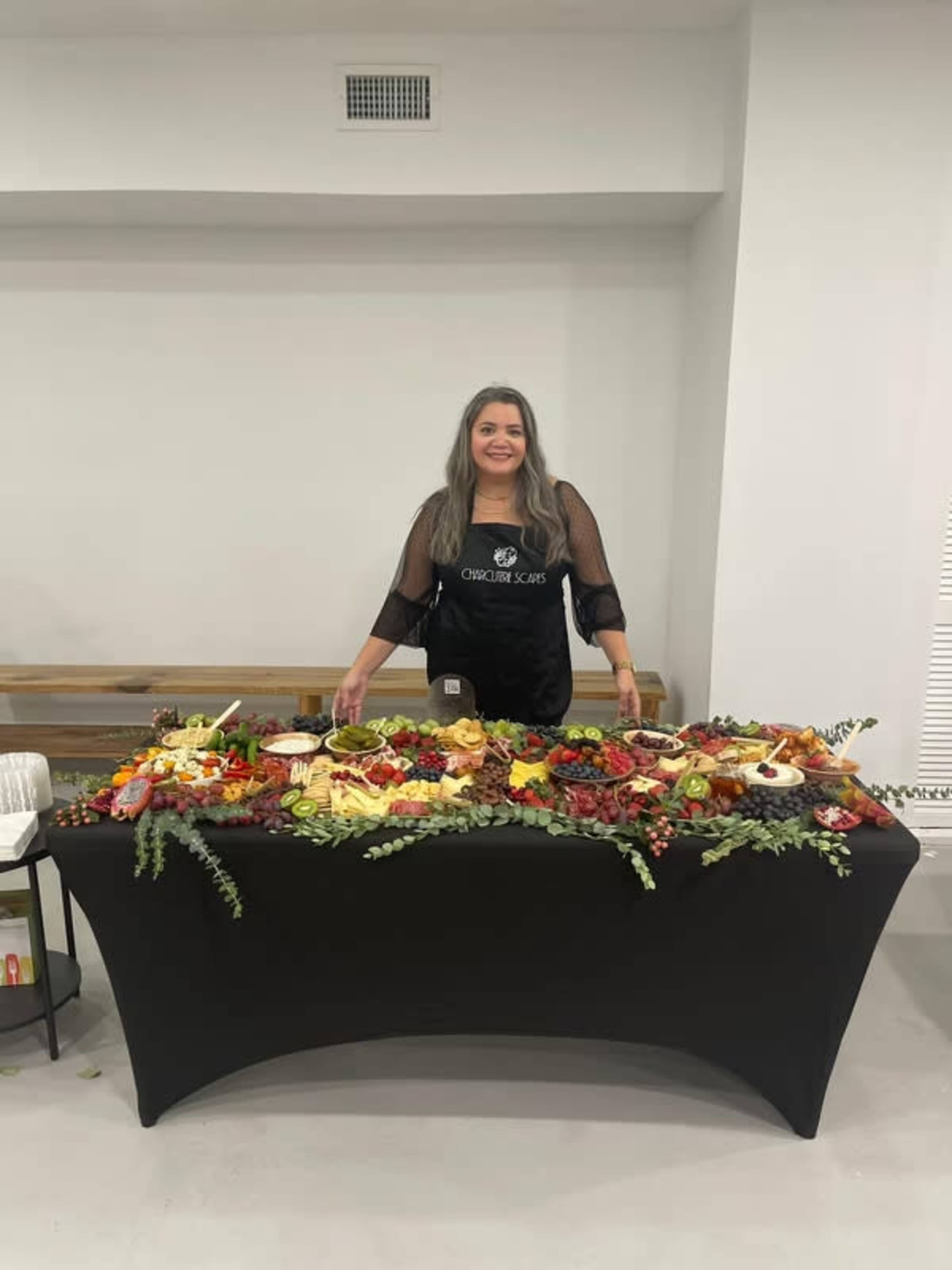 A person stands behind a large, decorated table filled with a variety of fruits, cheeses, and garnishes.