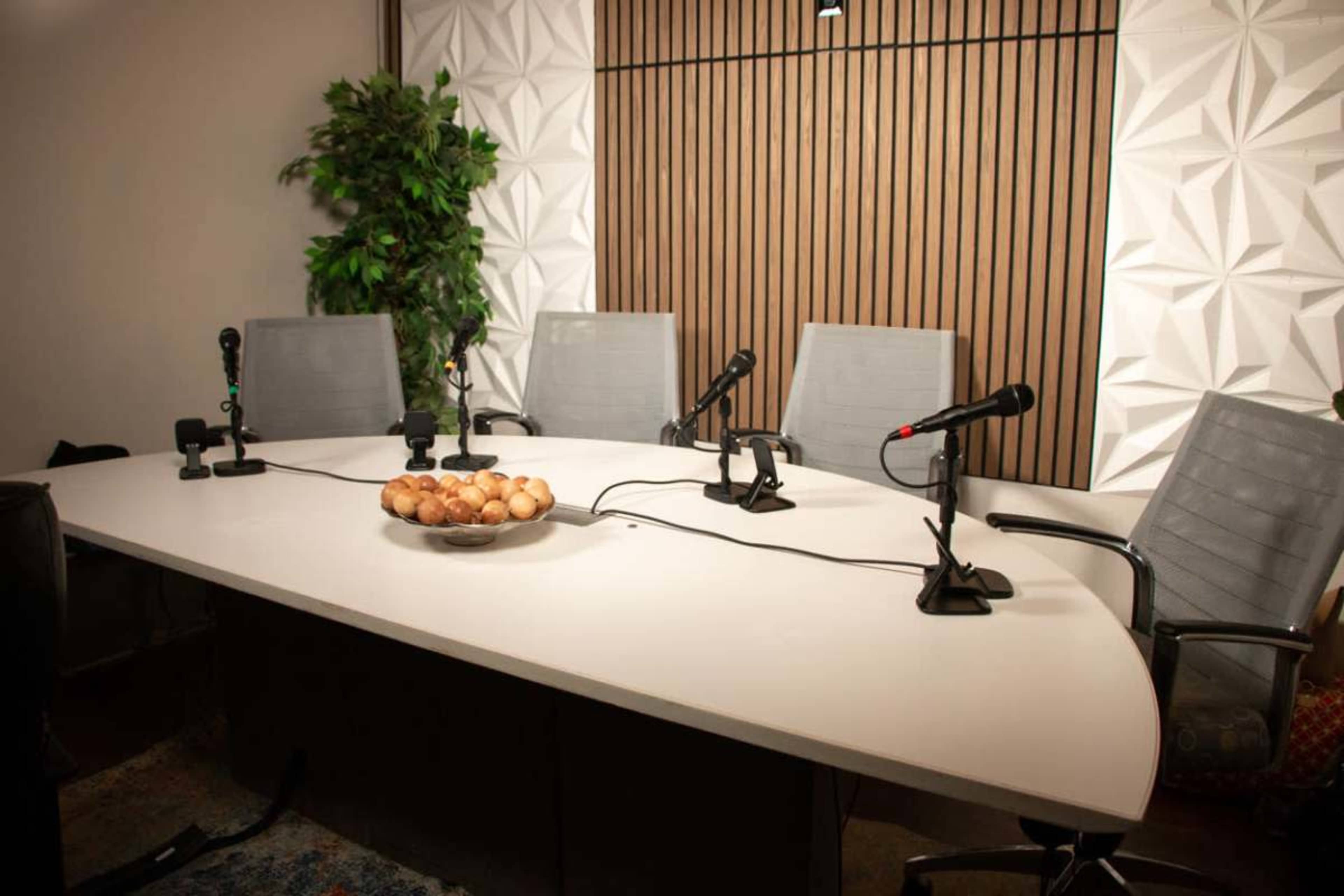 A modern conference room features a large white table with a bowl of eggs in the center, surrounded by high-backed chairs and positioned microphones.