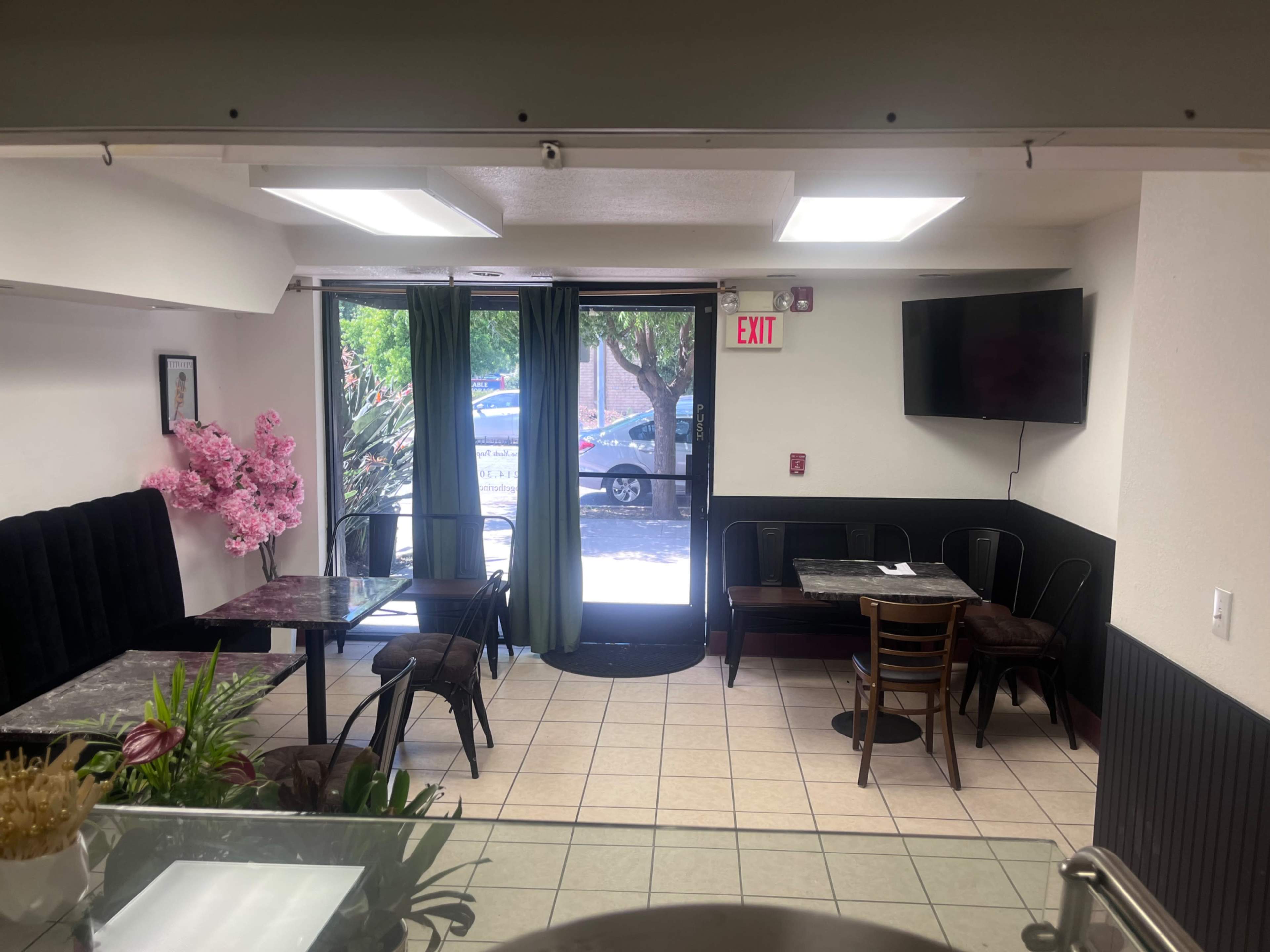 The image shows the interior of a small restaurant with black and white decor, featuring tables, chairs, and a glass door leading outside.