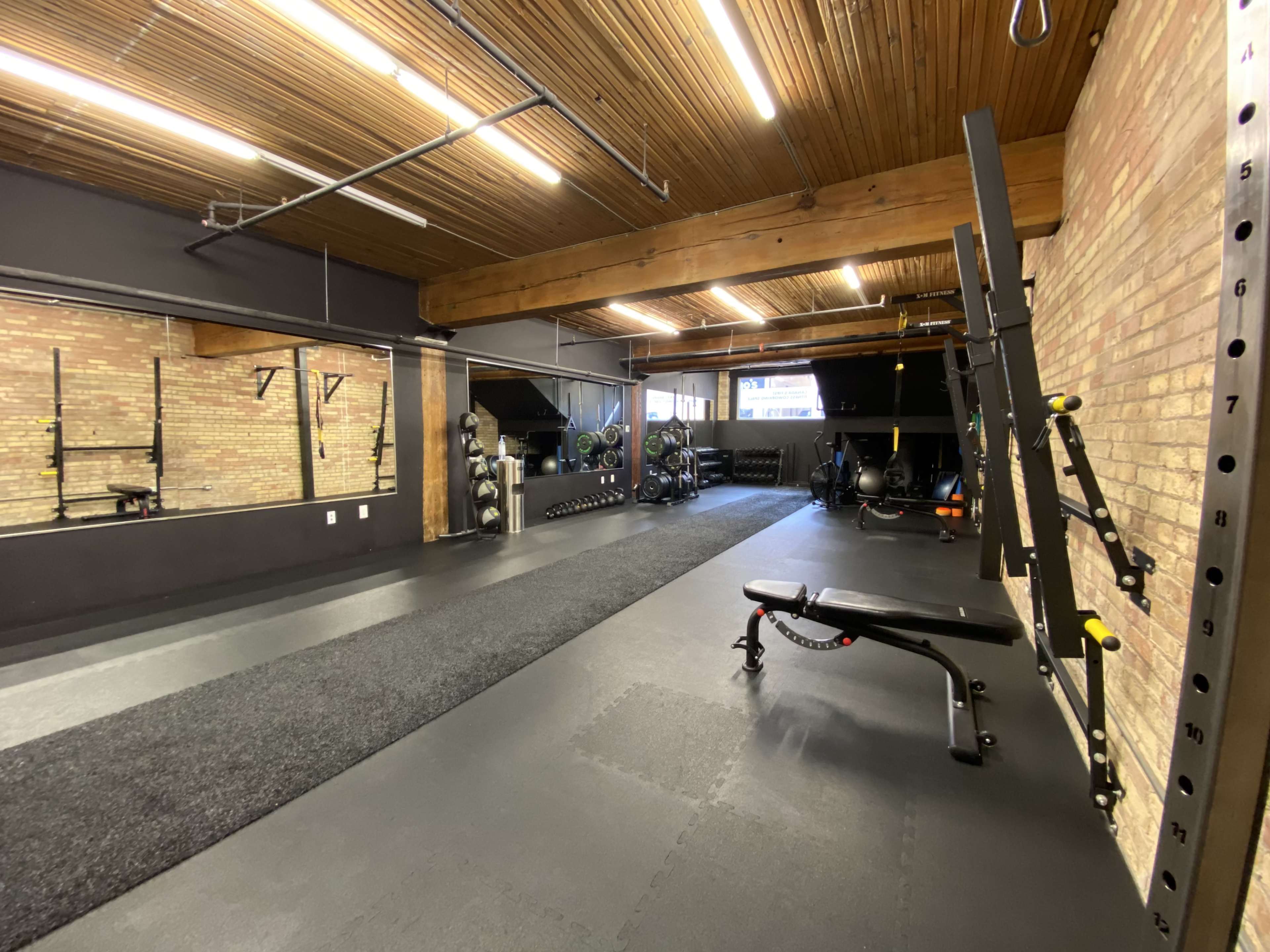 A spacious gym with wooden beams, brick walls, and various exercise equipment neatly arranged along the side.