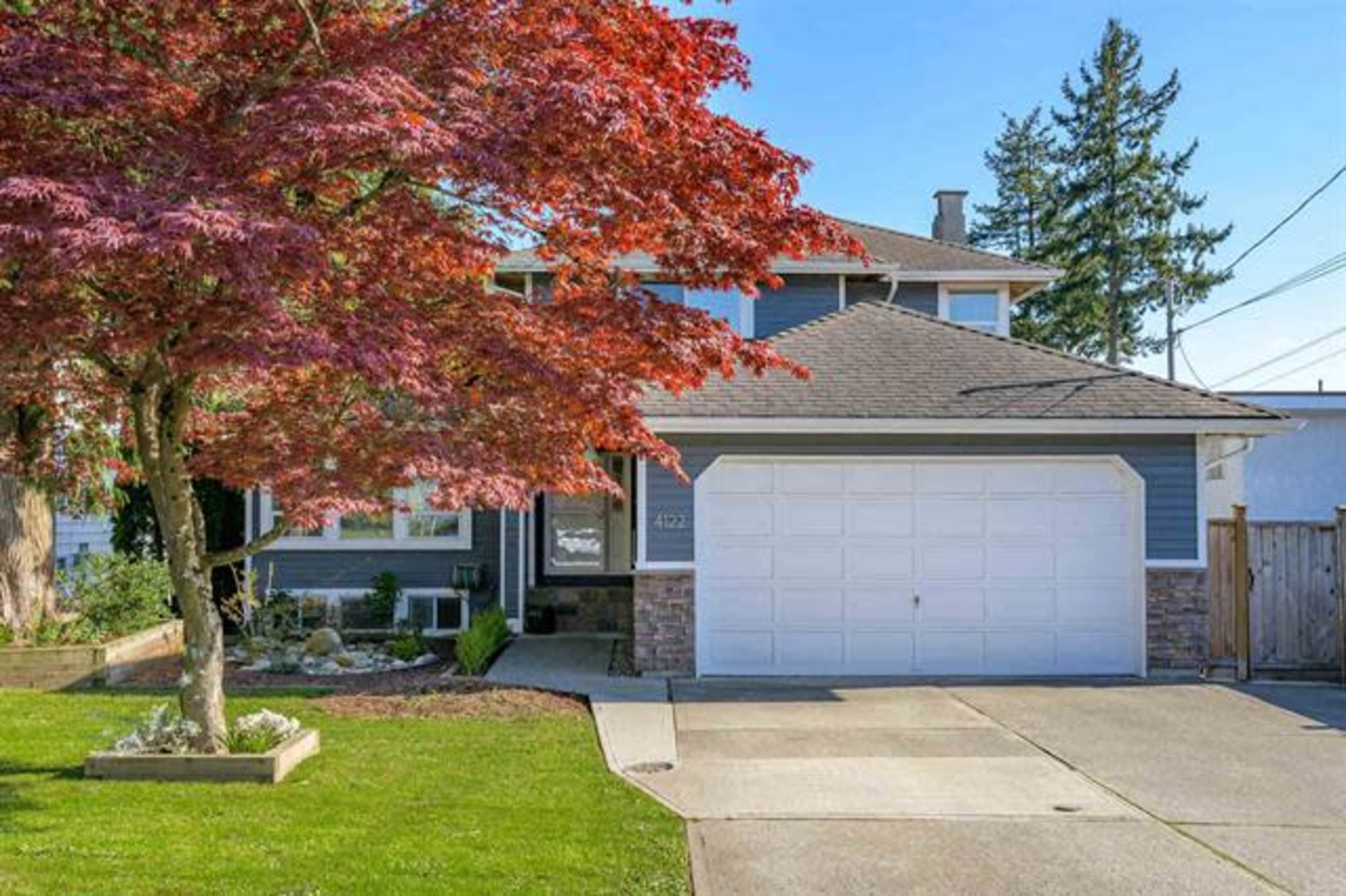 A two-story house with a gray exterior, a manicured lawn, and a red maple tree in the front yard.